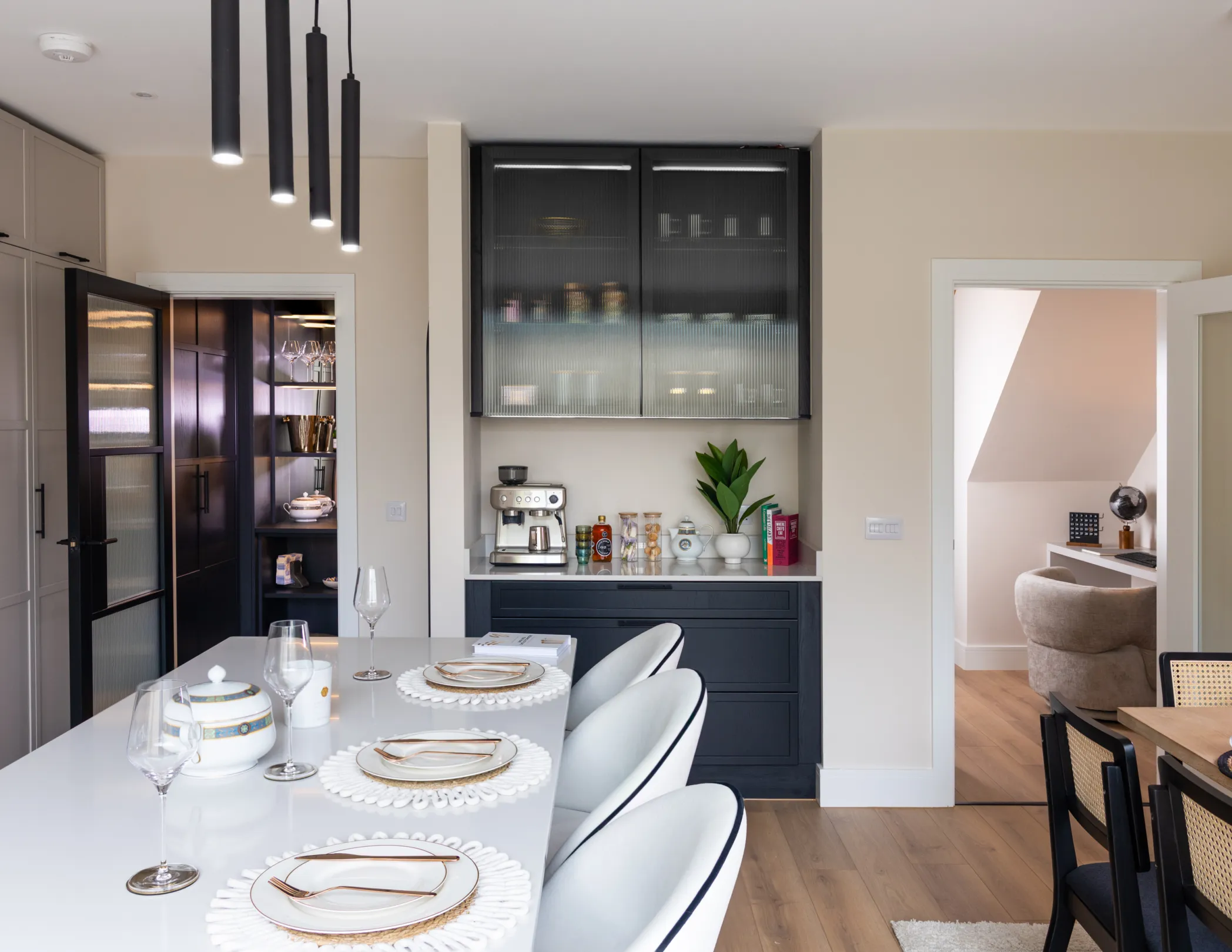 A bright, modern kitchen with a large island, dark cabinetry, and a glimpse into the pantry
