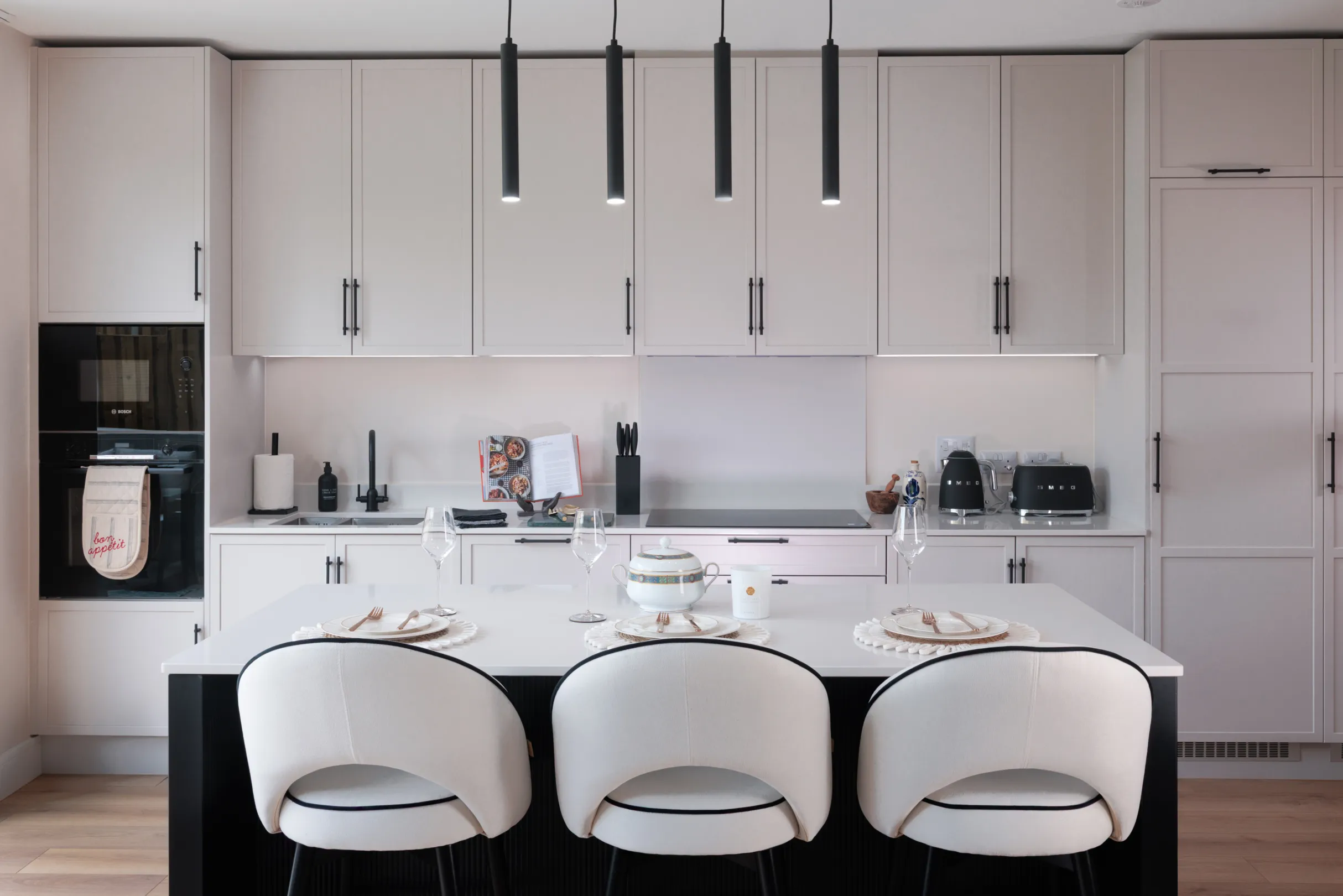 A modern, well-lit kitchen featuring white cabinets, black accents, a central island with bar stools, and sleek lighting fixtures.