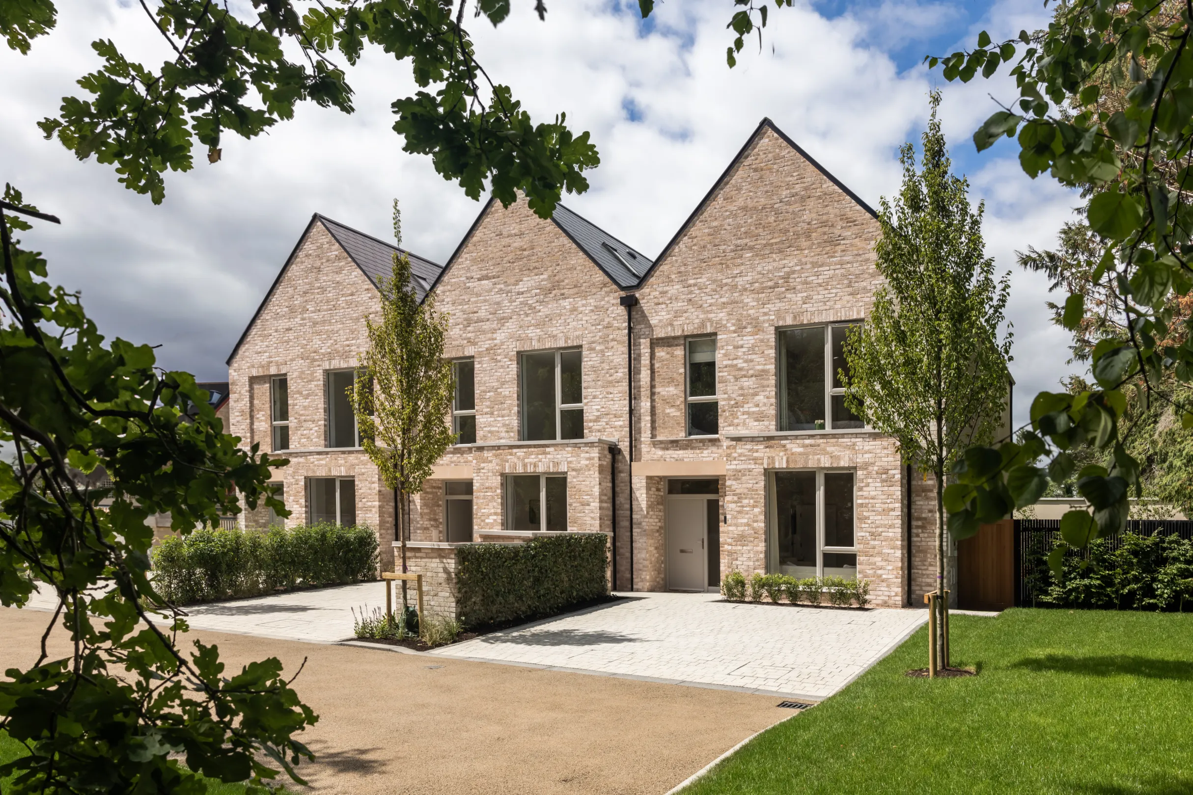 Two modern brick houses stand side-by-side with symmetrical designs and greenery enhancing the surrounding landscape.