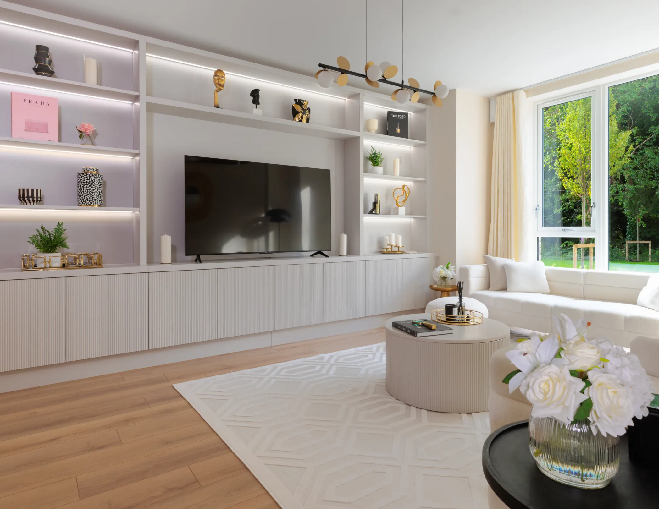 A well-lit living room features a large built-in entertainment center, a comfortable white sofa, and a stylish rug, creating a modern and inviting space.