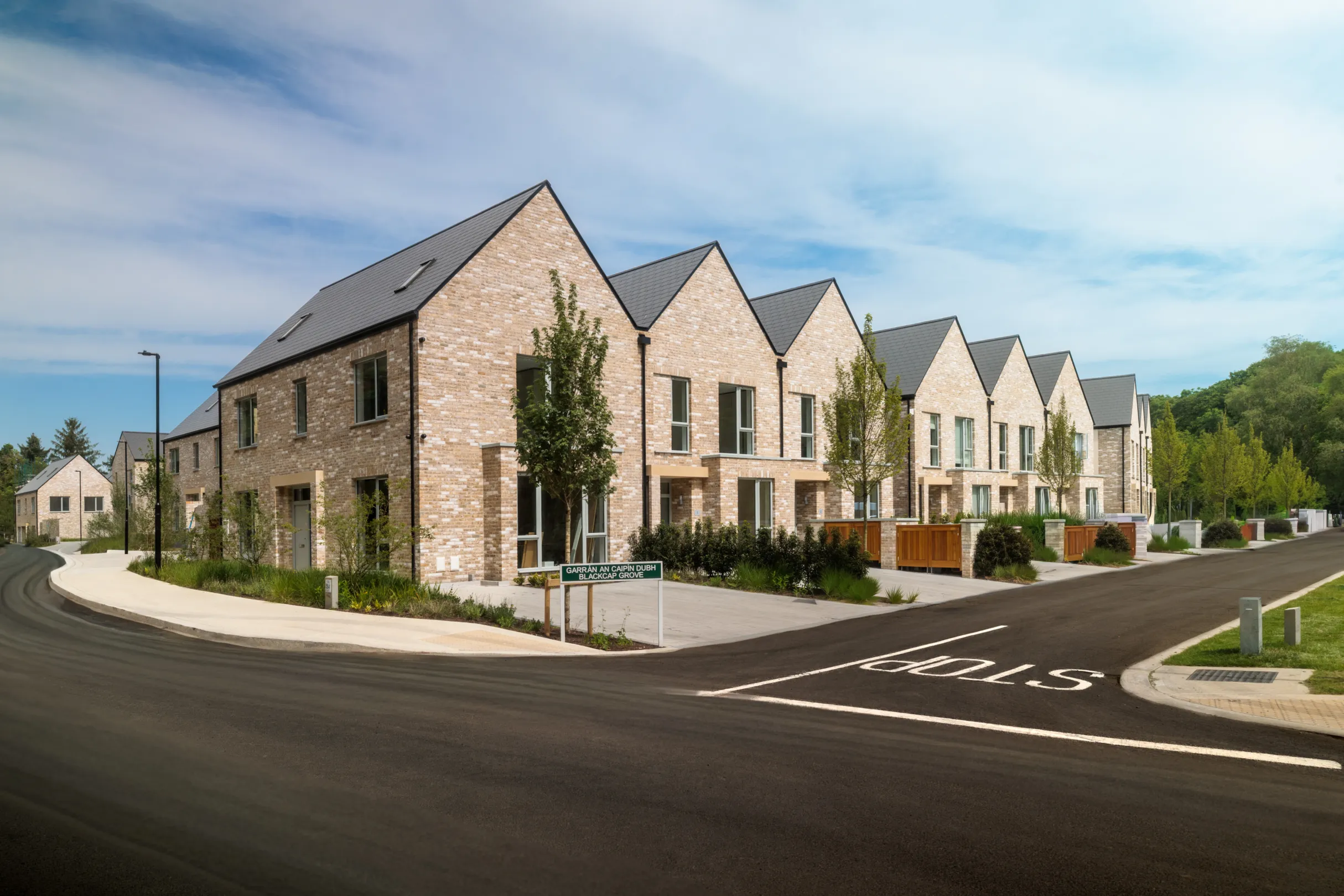 A row of modern terraced houses with landscaping and cars in the driveway