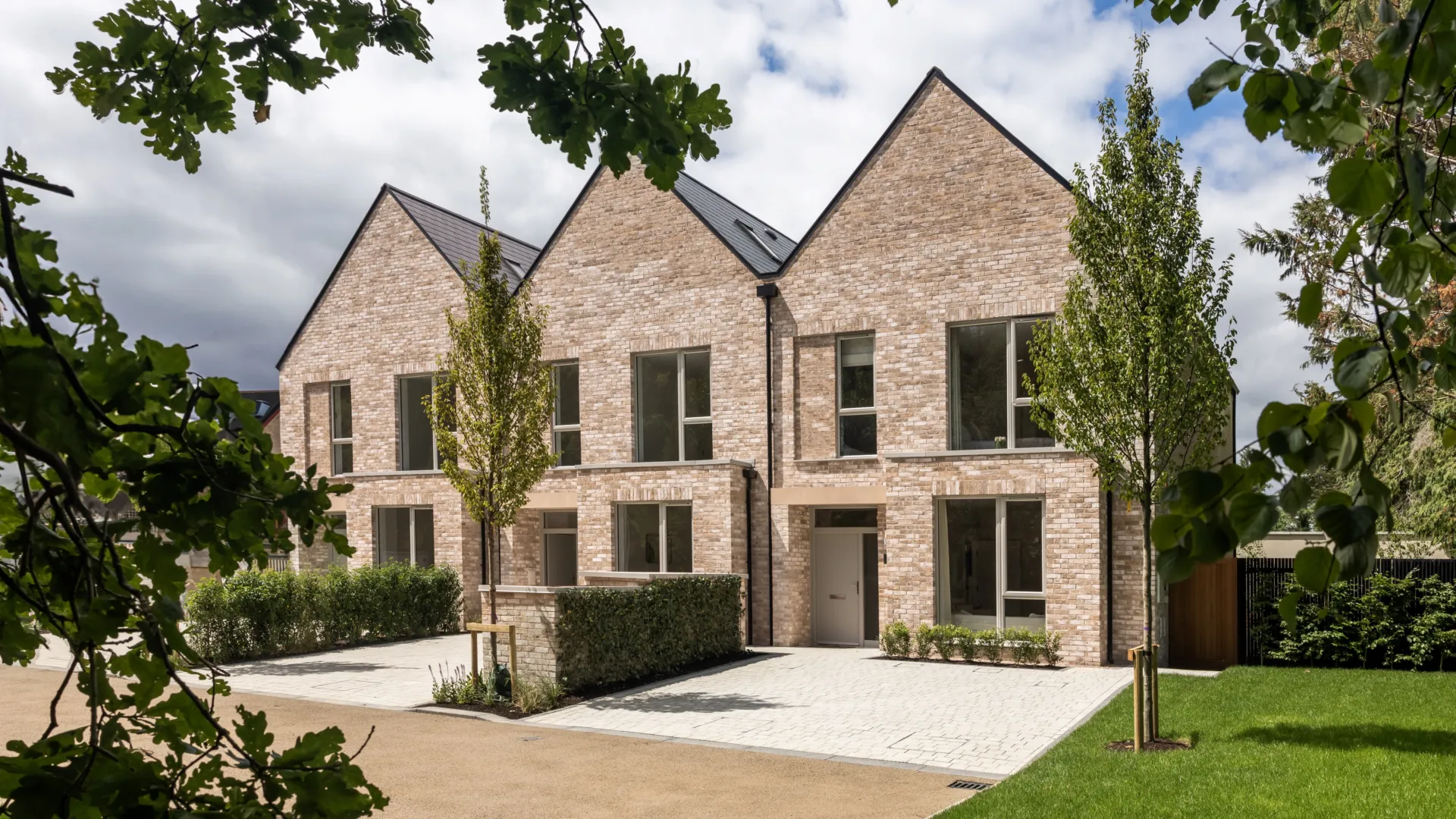 Two modern brick houses stand side-by-side with symmetrical designs and greenery enhancing the surrounding landscape.