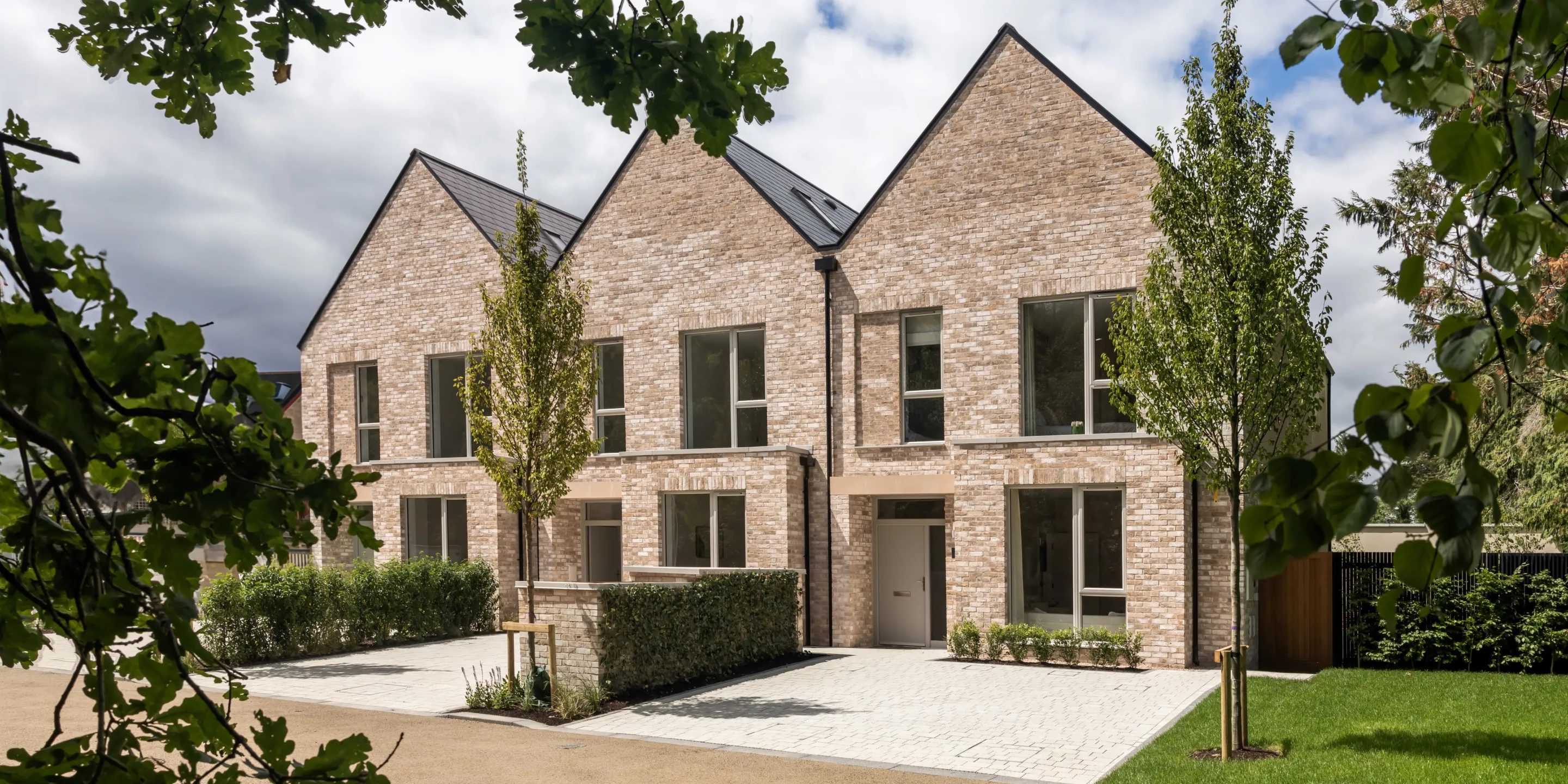 Two modern brick houses stand side-by-side with symmetrical designs and greenery enhancing the surrounding landscape.