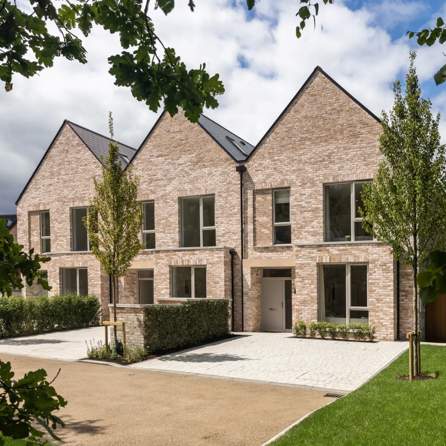 Two modern brick houses stand side-by-side with symmetrical designs and greenery enhancing the surrounding landscape.