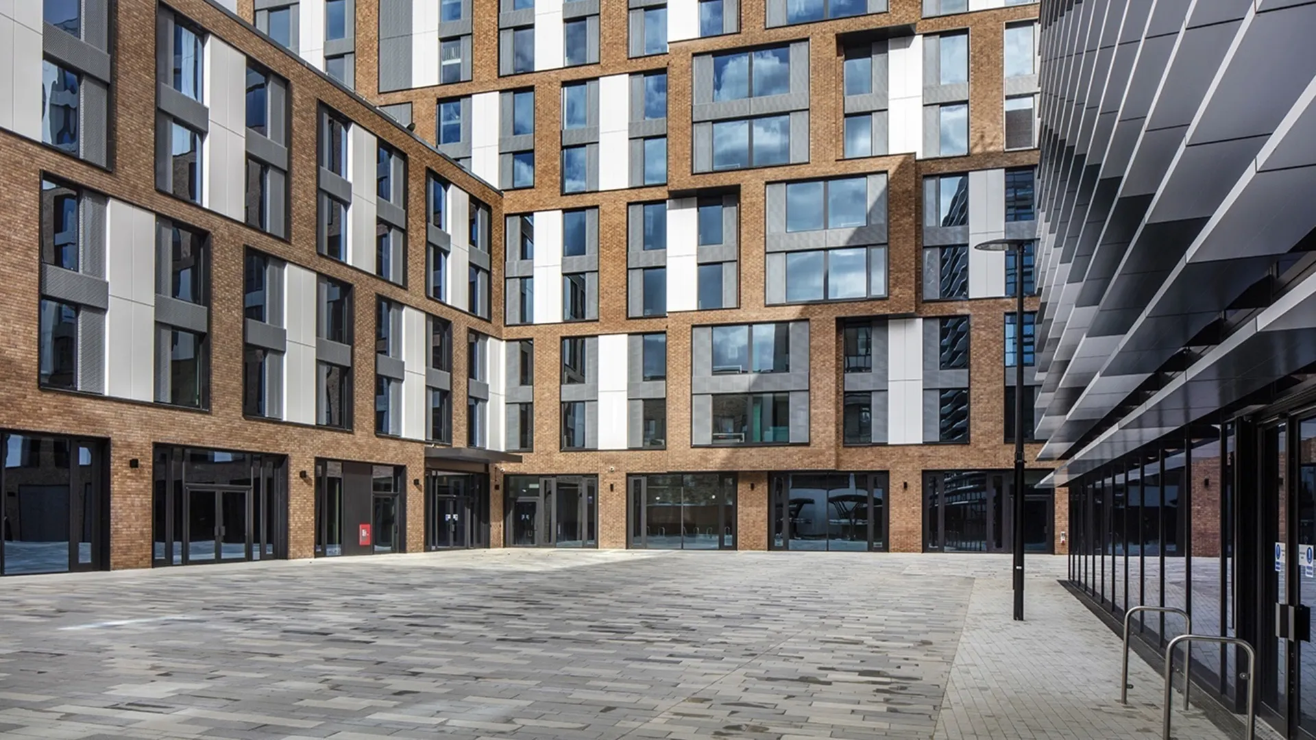 The courtyard of a modern multi storey building with solar shading detail on the right hand side and brick paving in the centre
