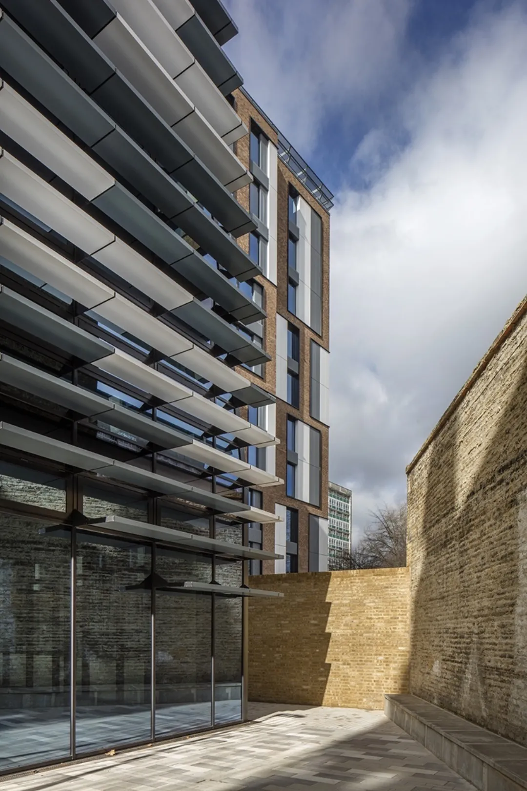 A modern building with solar shading contrasting with older stock brick walls that adjoin the development