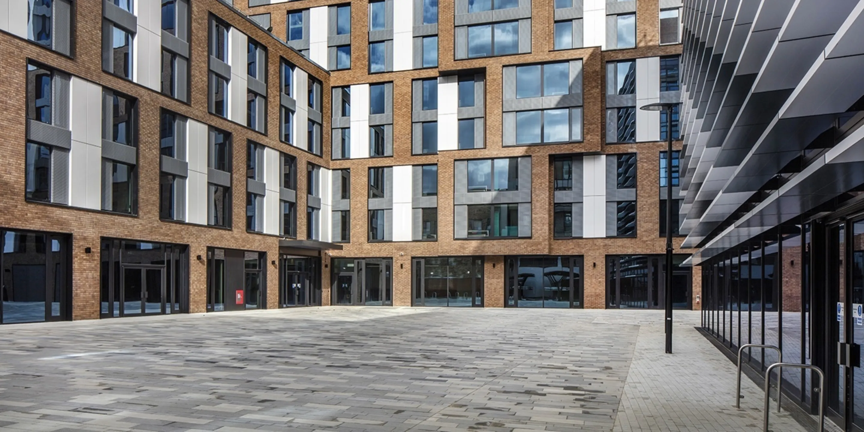 The courtyard of a modern multi storey building with solar shading detail on the right hand side and brick paving in the centre