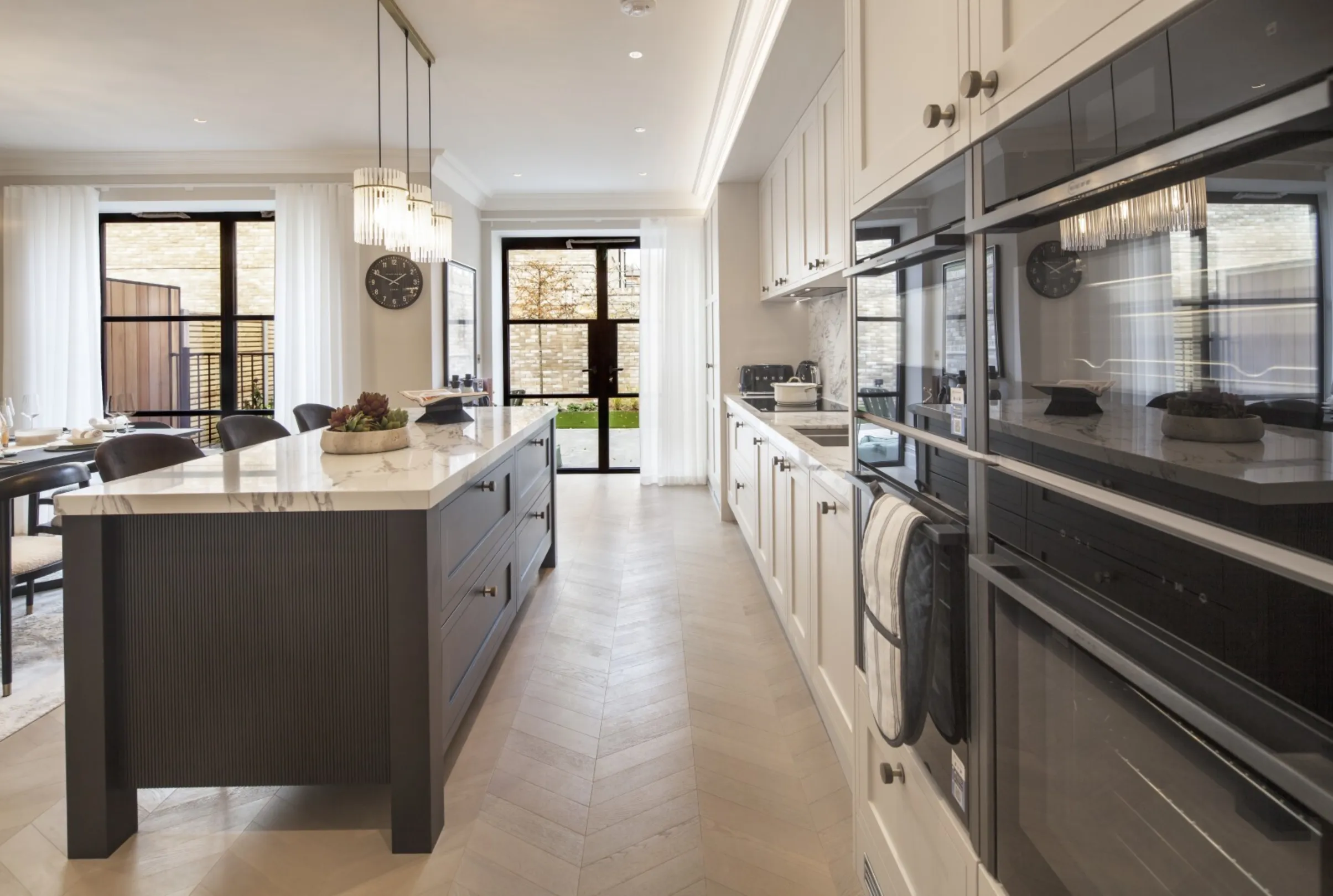 Kitchen (galley view): Integrated appliances and chevron oak flooring lead the eye through to the garden beyond.