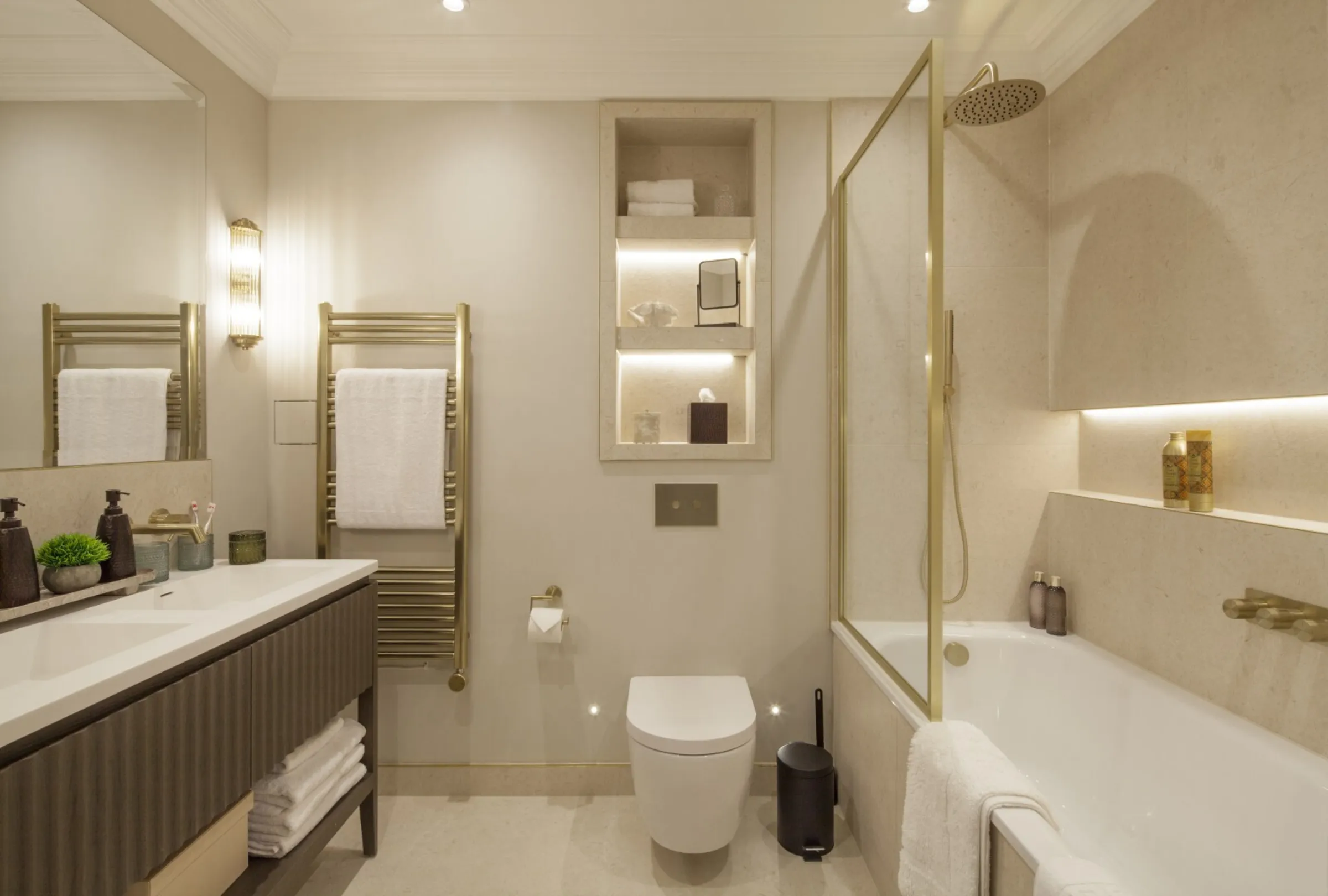Family bathroom: A serene stone-tiled bathroom with rainfall shower, heated brass towel rails and illuminated niches.