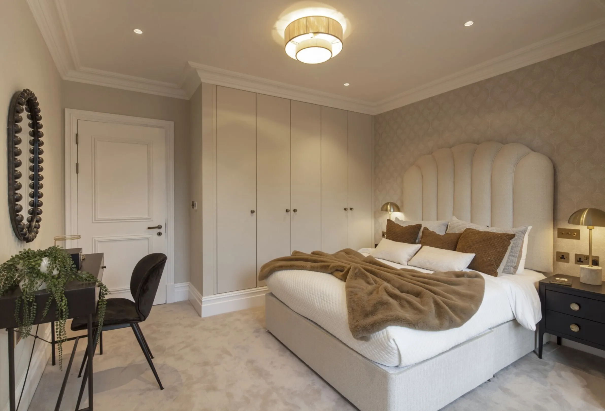 Second bedroom (bed view): A scalloped upholstered headboard, floor-to-ceiling fitted wardrobes and soft brass lighting create a serene, hotel-inspired retreat.