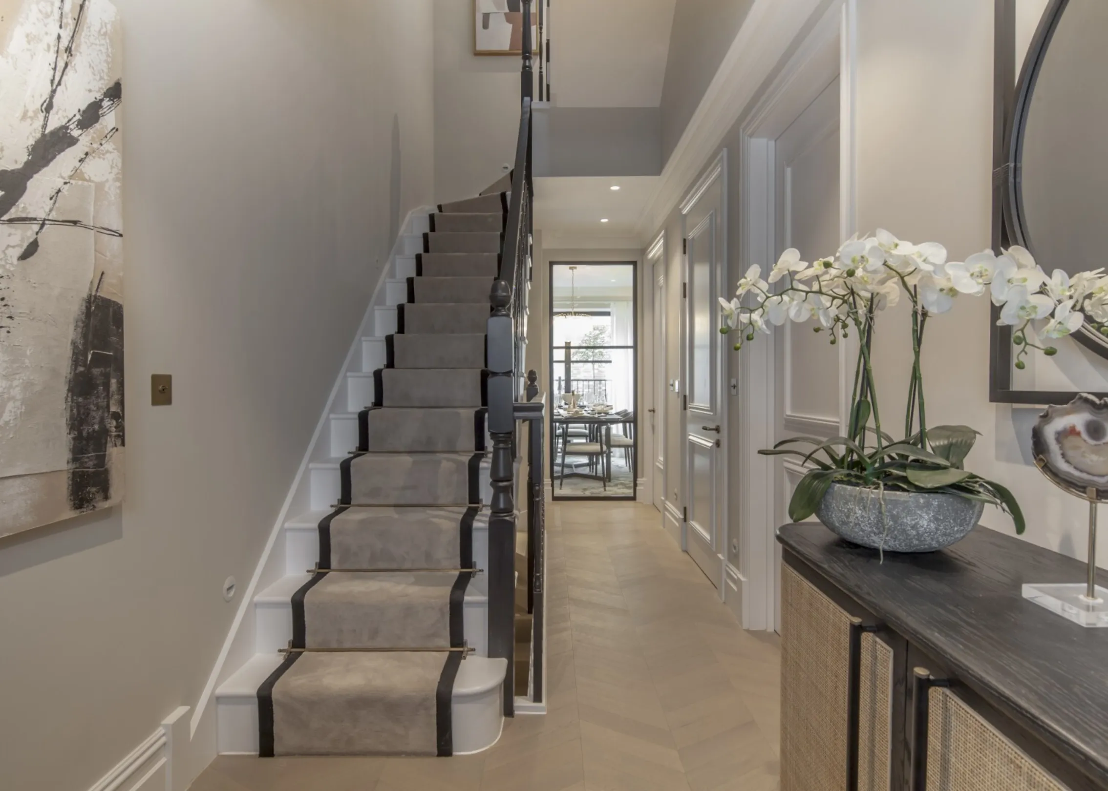 Entrance hall: A welcoming hallway with chevron oak flooring, panelled walls and a classic stair runner, leading through glazed doors to the kitchen and dining space.