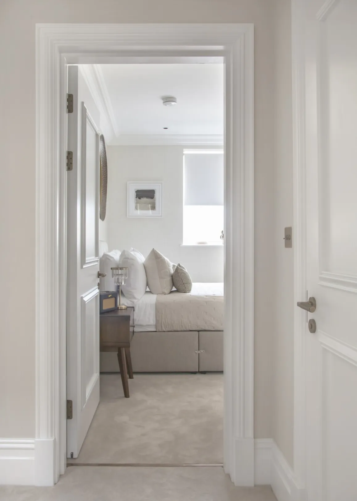 Guest bedroom (doorway view): Panelled doors and deep architraves frame a glimpse into a calm, softly neutral double bedroom.