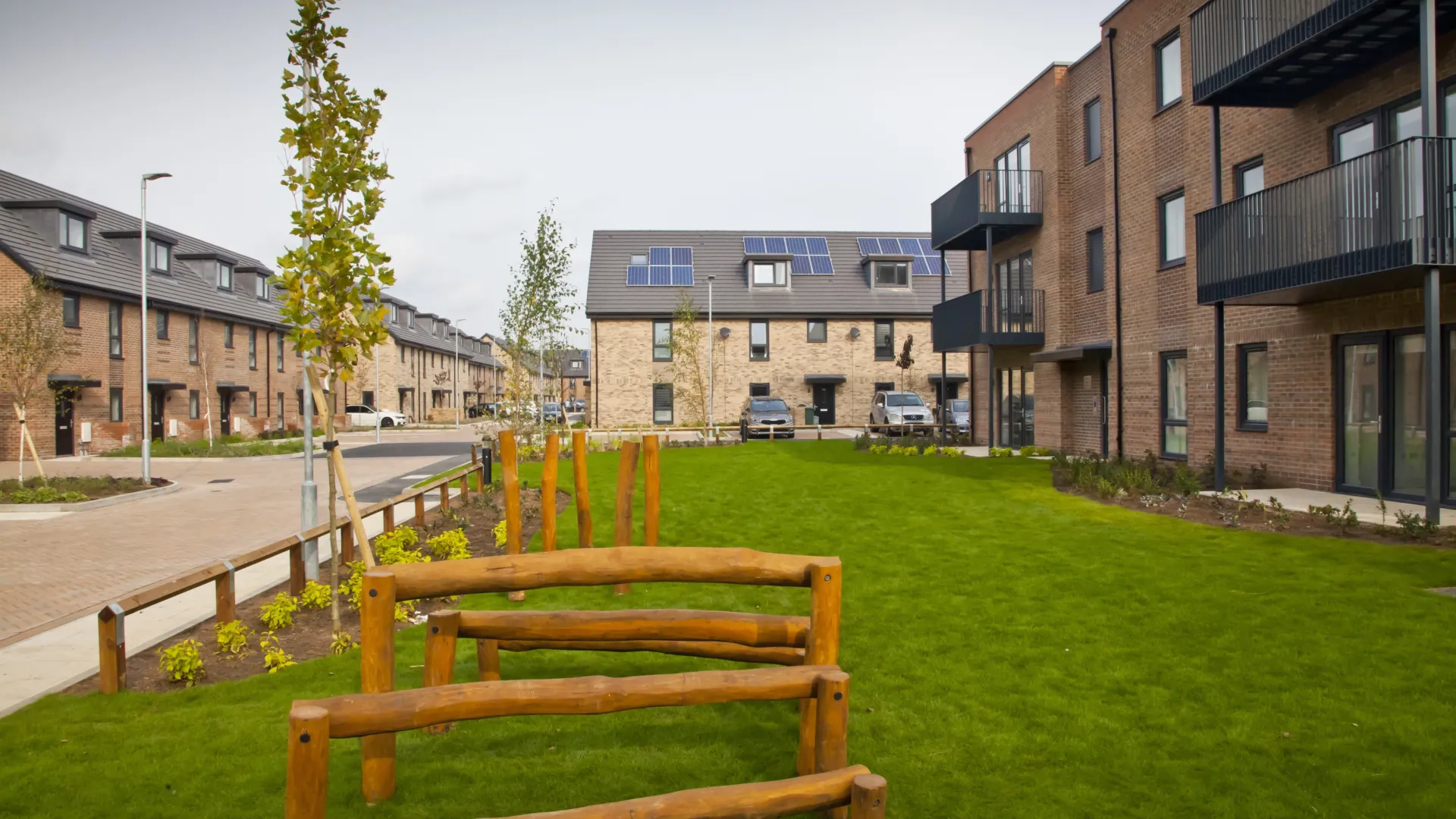 Modern terraced homes built in brick and low rise flats forming the same development surround a central green space.