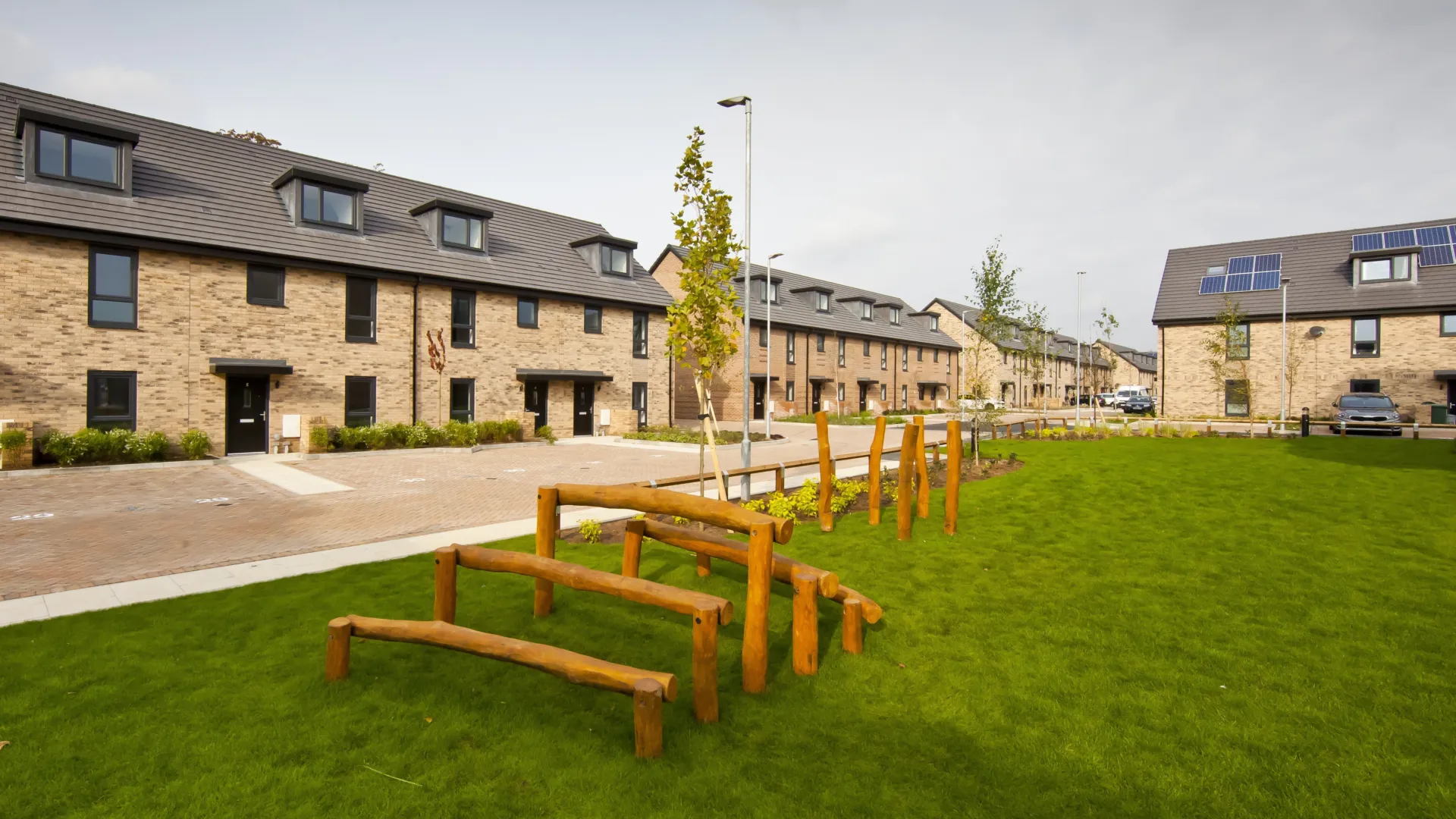 Multiple modern terraced homes built in brick with dormer windows, parking in front and a central green space