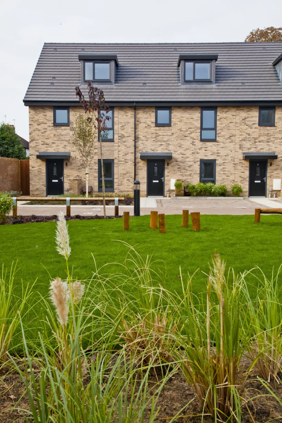 Three modern terraced homes built in brick with dormer windows, seen from a central green space