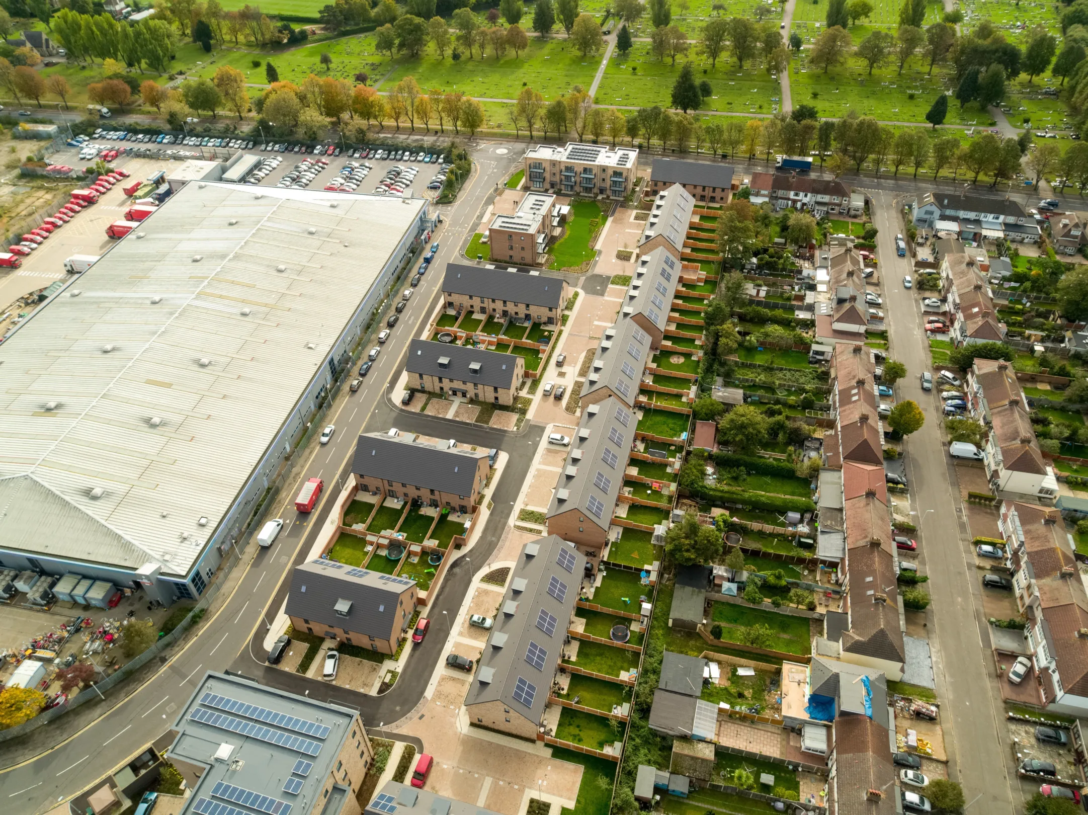 Arial view of multiple rows of modern terraced homes built in brick with dormer windows, parking in front and gardens to the rear