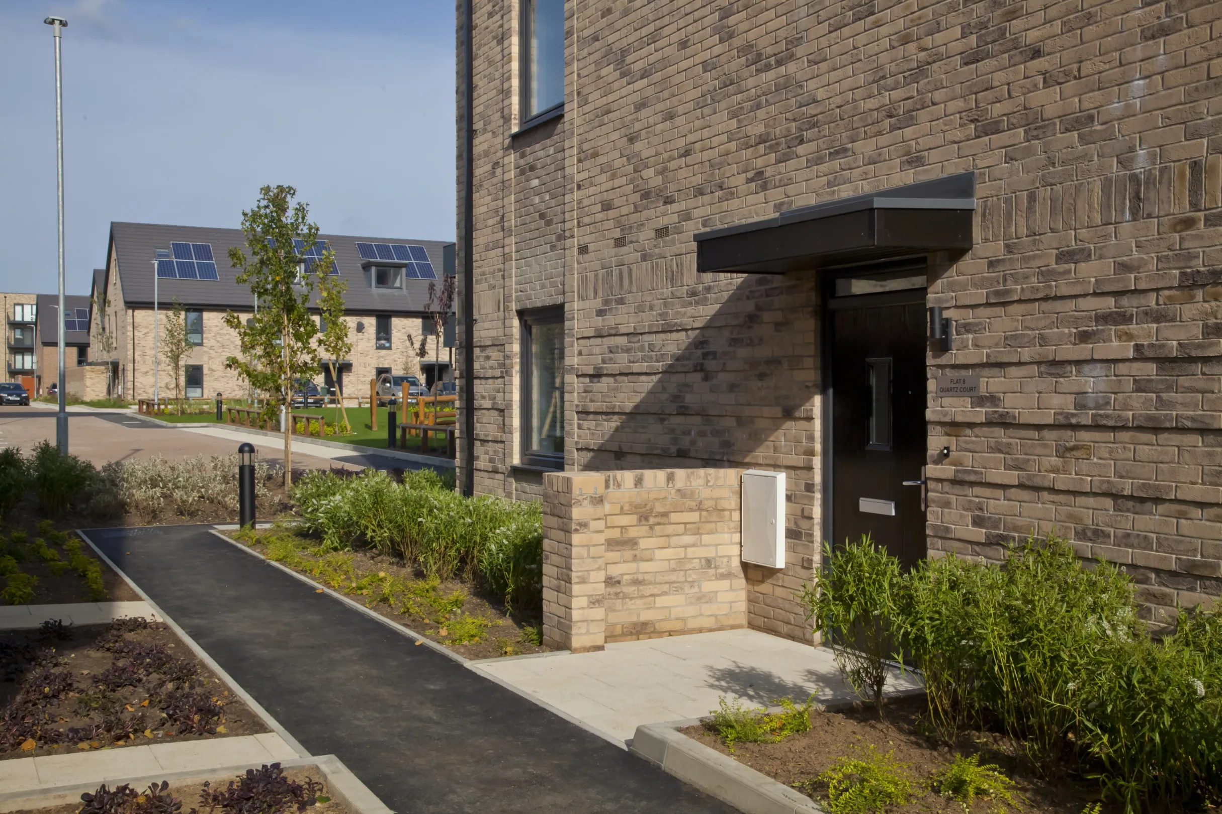 Three modern homes built in brick showing pedestrian walk ways between front doors and planting in small front gardens