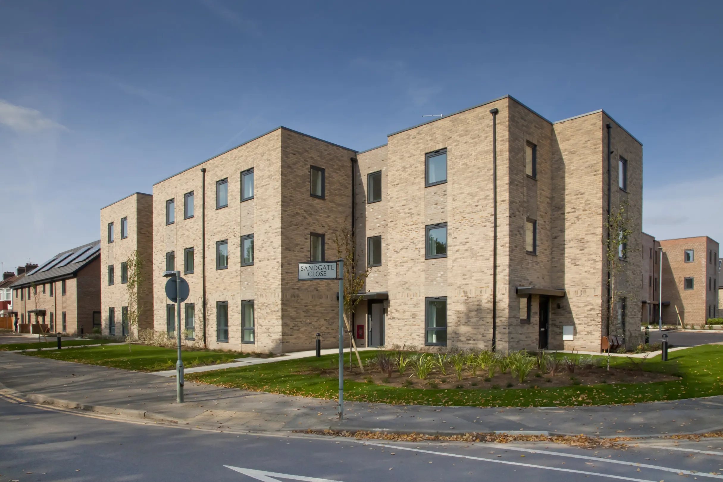 Modern low-rise flats in a residential development overlooking green space around the perimeter, with single family homes of the same development in the background