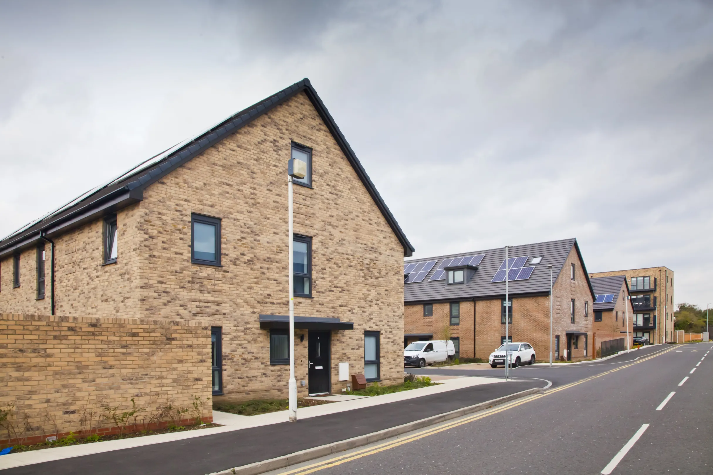 Modern terraced homes built in brick with walled rear gardens and solar panels on the roof. Flats forming part of the same development are in the distance.
