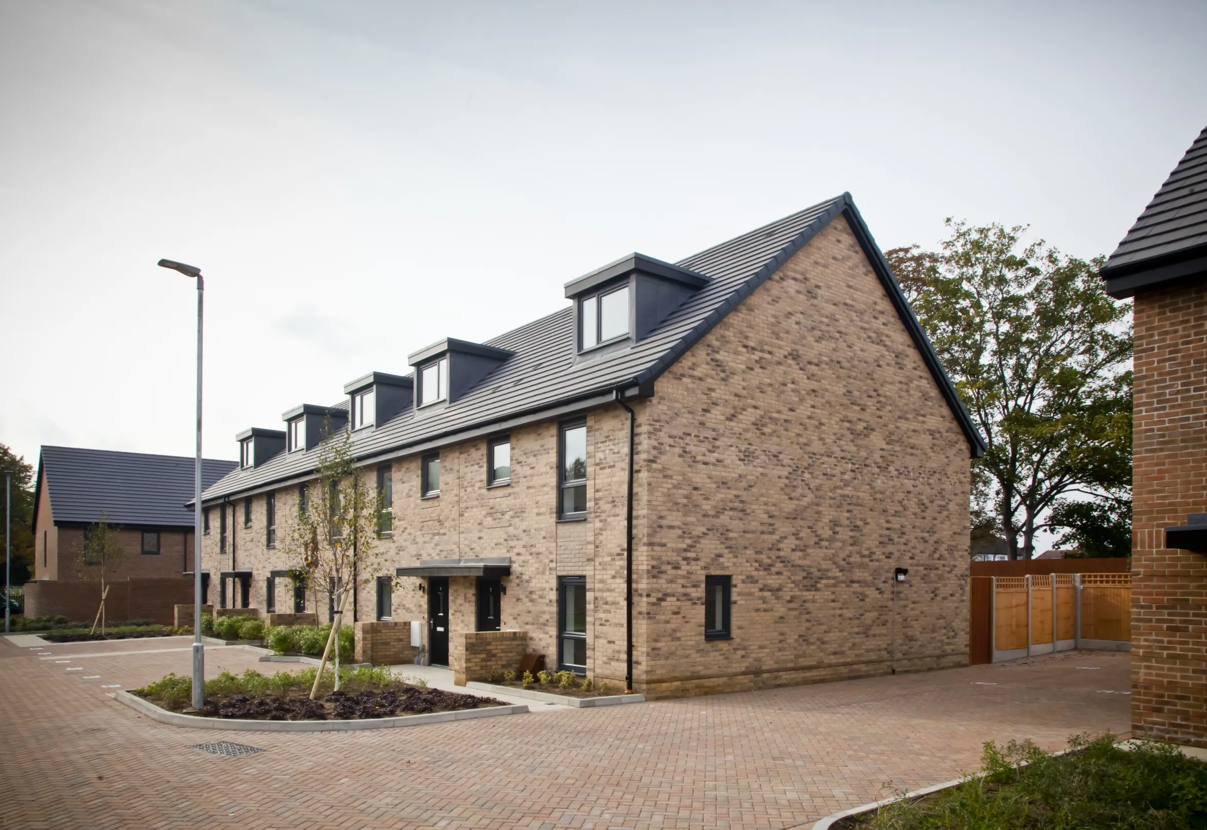 Modern terraced homes built in brick with dormer windows in the roofs and off street parking.