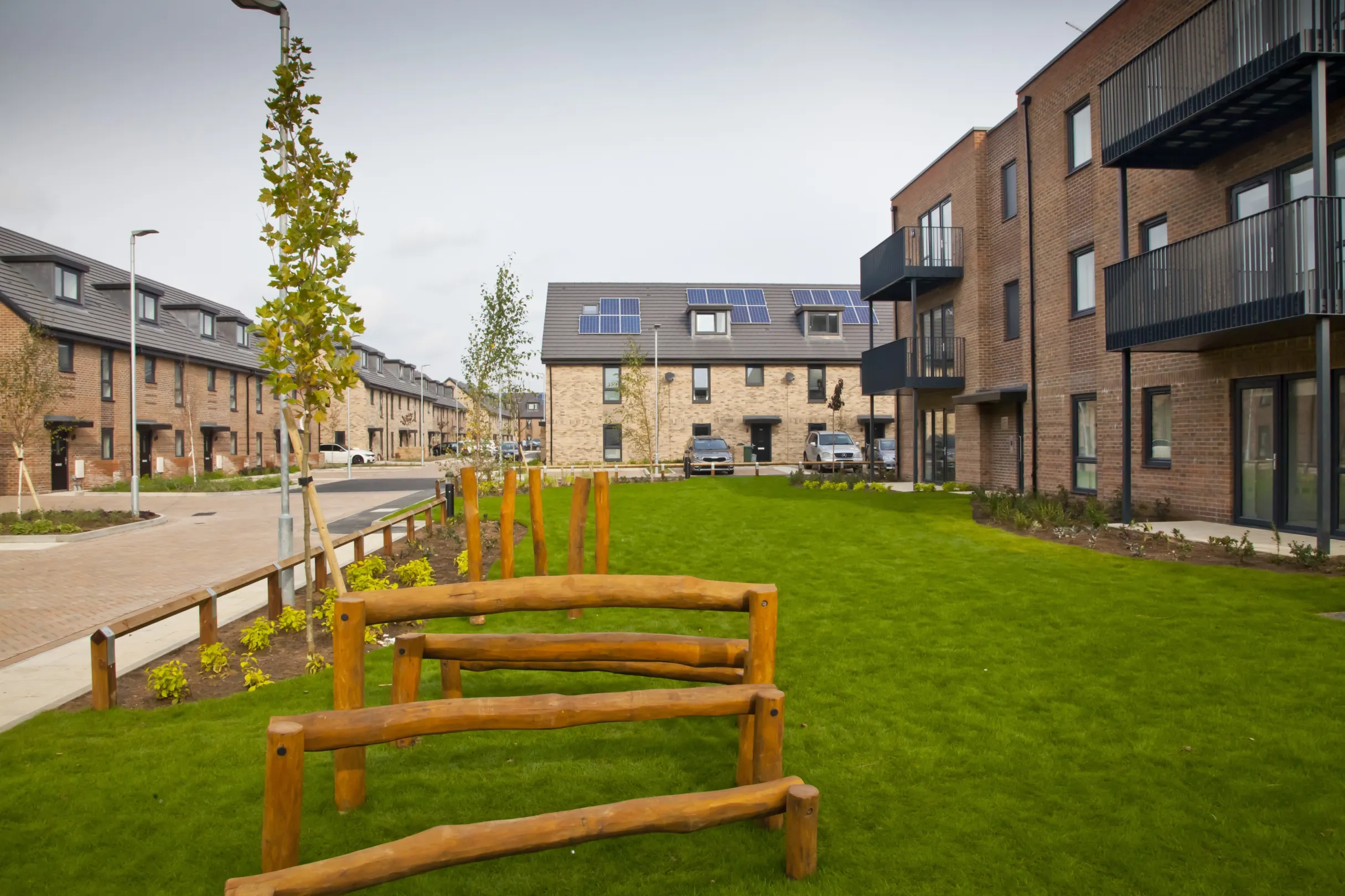 Modern terraced homes built in brick and low rise flats forming the same development surround a central green space.