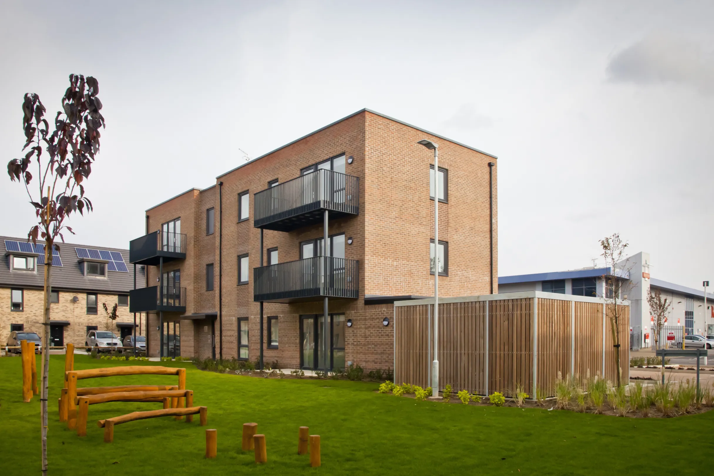 Modern flats low-rise flats overlook a communal green space at the centre of a residential development. Houses in the same development are in the background.
