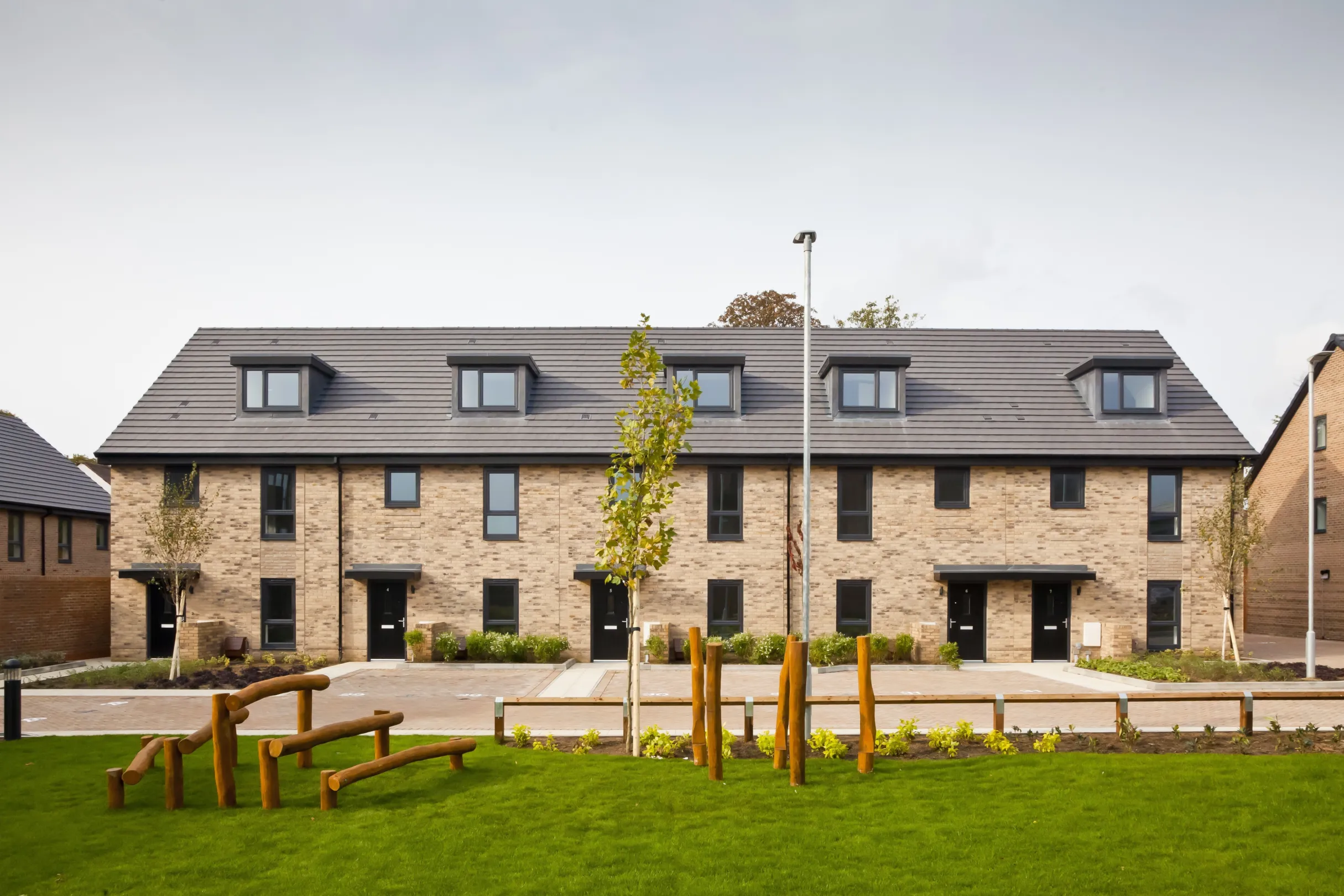 Modern terraced brick homes with dormer windows overlook a communal green space at the centre of a residential development