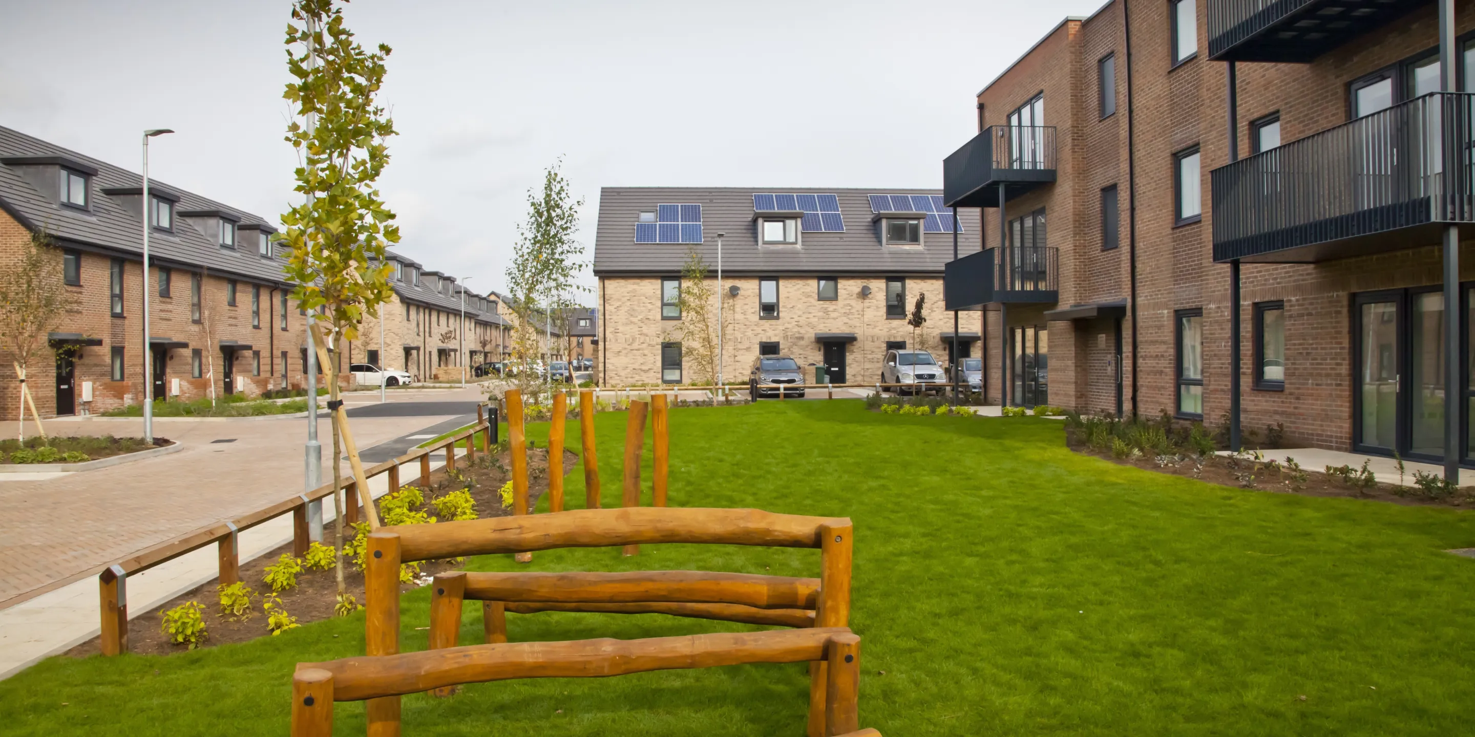 Modern terraced homes built in brick and low rise flats forming the same development surround a central green space.