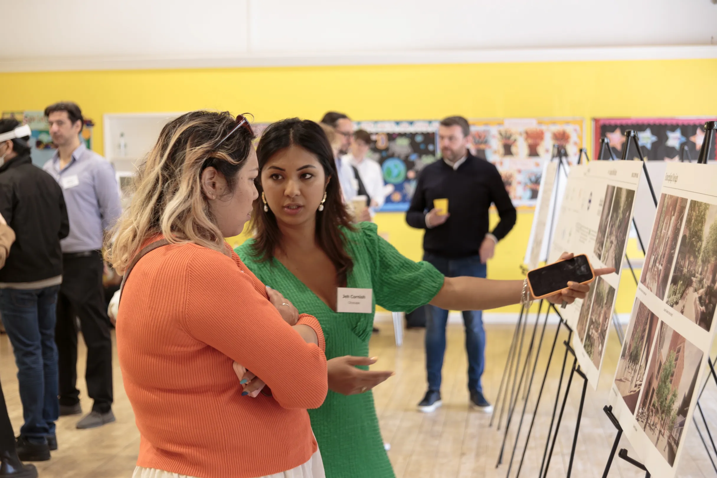 A public consultation in a local community hall, a lady pointing to an illustration board of a development discussing it with a local resident