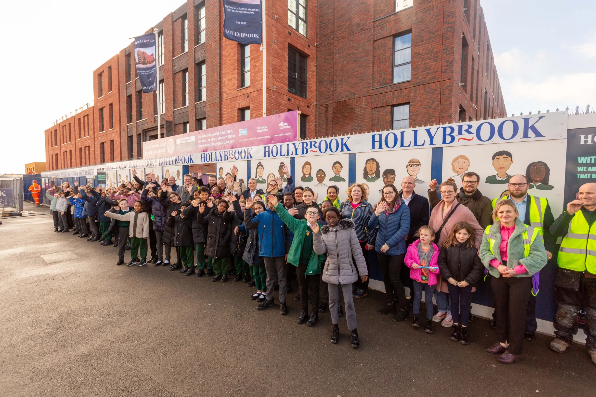 Primary school children, teacher and Hollybrook staff stand and wave in front of a newly constructed residential building