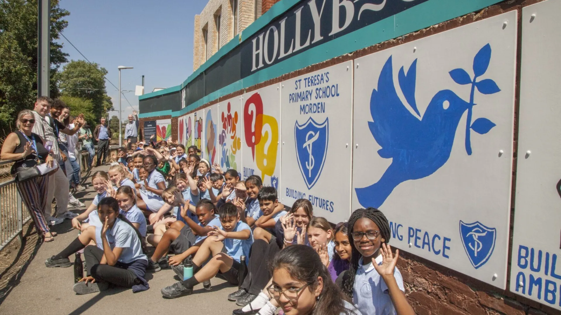 School children at the Hollybrook construction site in Wimbledon, sitting next to their artwork which is displayed along the brickwall next to Merton Tram Stop