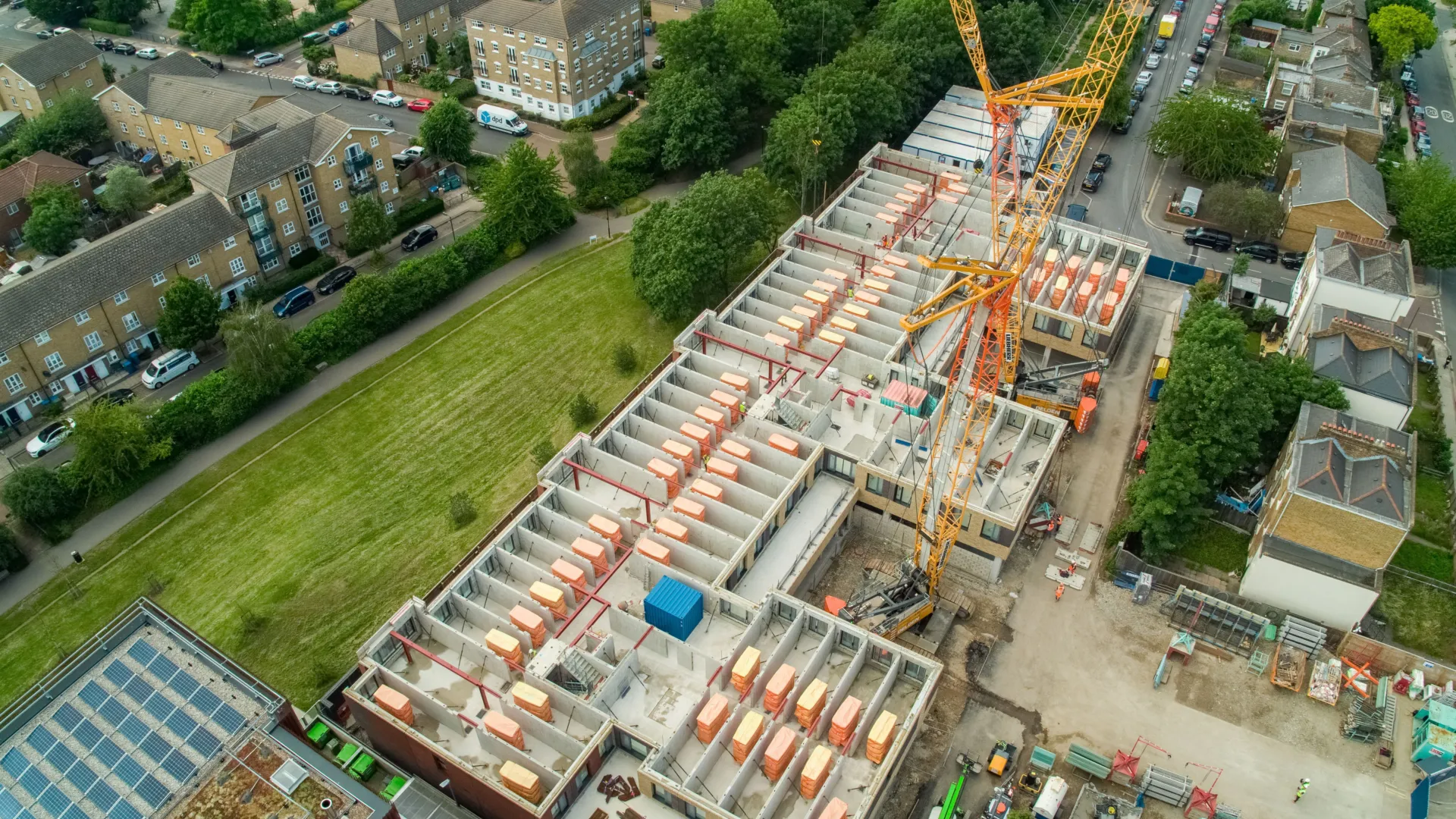 A large construction site with a crane dominates the frame, surrounded by green spaces and residential buildings.
