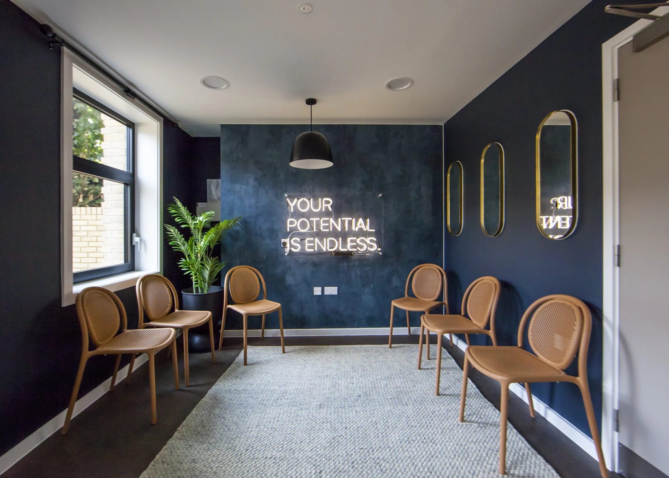 Seated area with a neon sign reading "your potential is endless", door and mirrors on the right wall, a large window on the left.