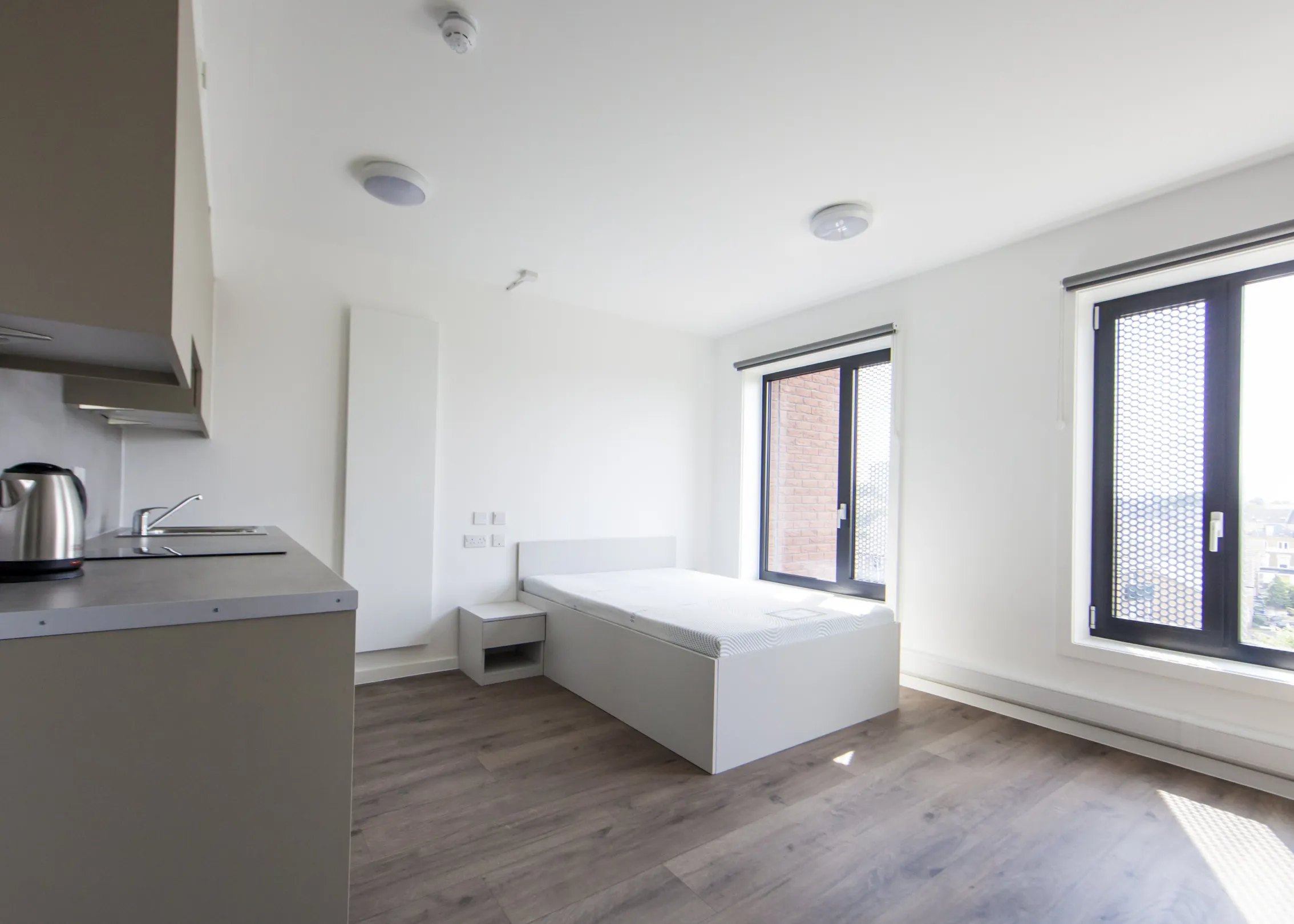 A kitchen area and bed against the wall with two windows looking out.