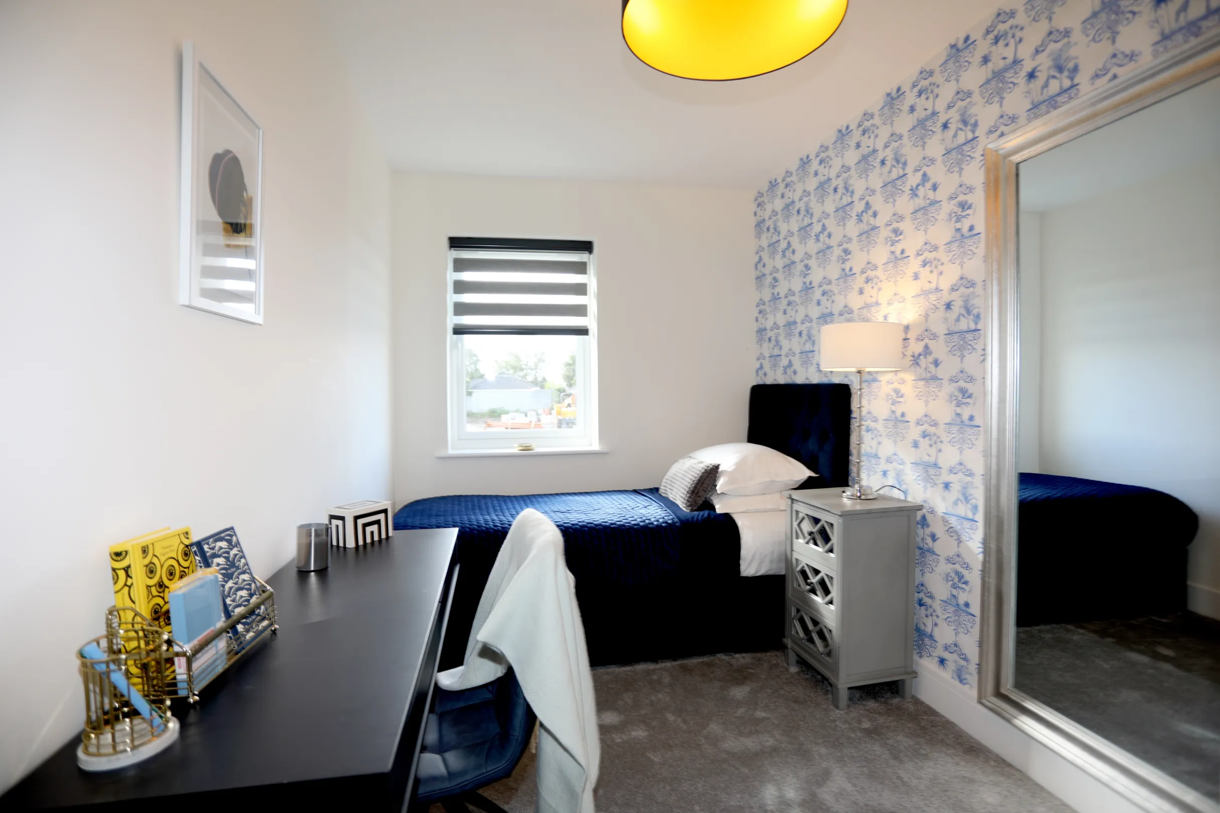 A single bedroom with white and navy wallpaper on a feature wall, navy bed through, black dressing table