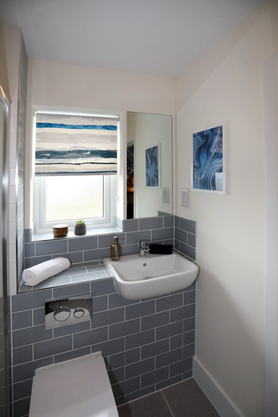 A master ensuite with light blue brick tiles, a white basin and WC, with a large mirror above the basin