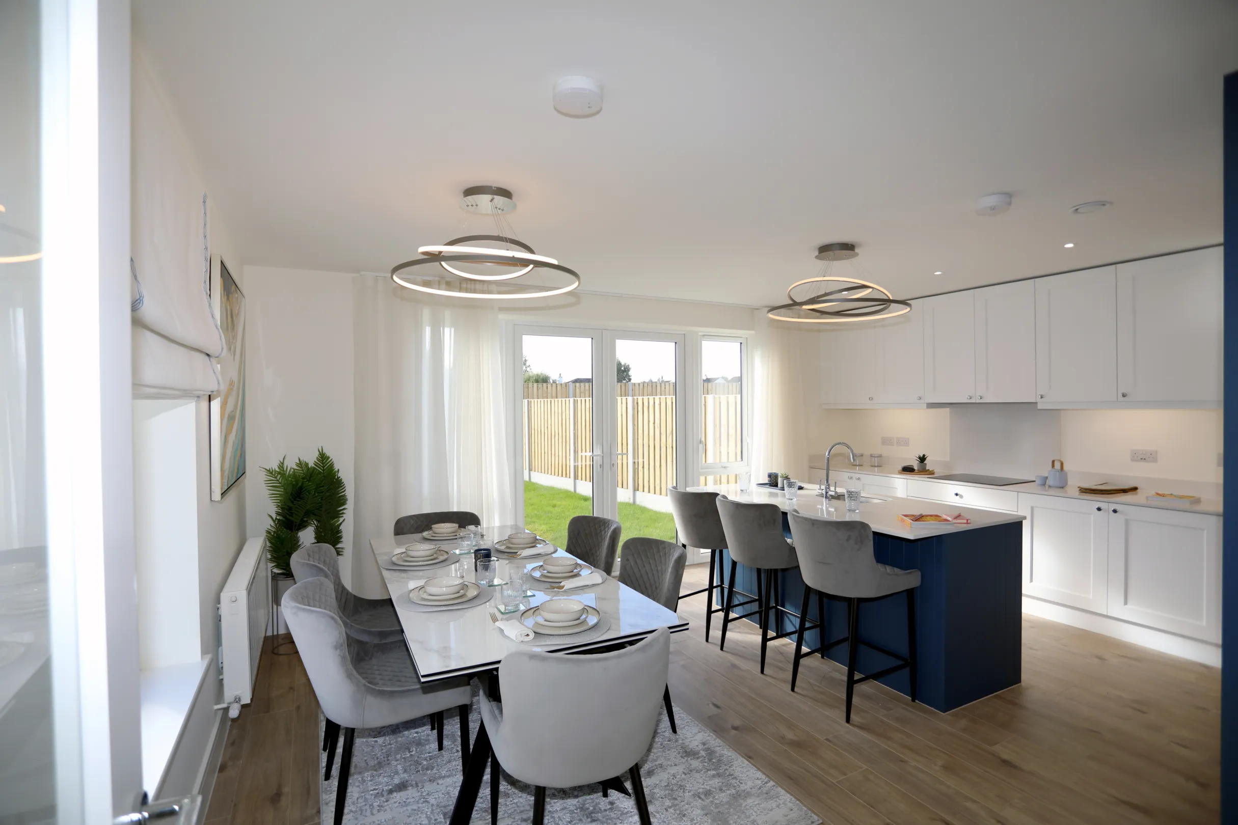 A modern kitchen dining room, a navy and white kitchen with central island unit, dining table set with plates and cutlery with grey dining chairs