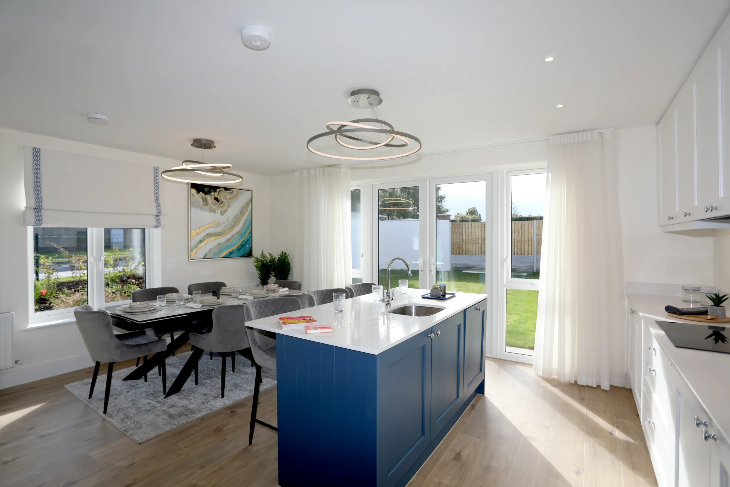 A modern kitchen dining room, a navy and white kitchen with central island unit, dining table set with plates and cutlery with grey dining chairs