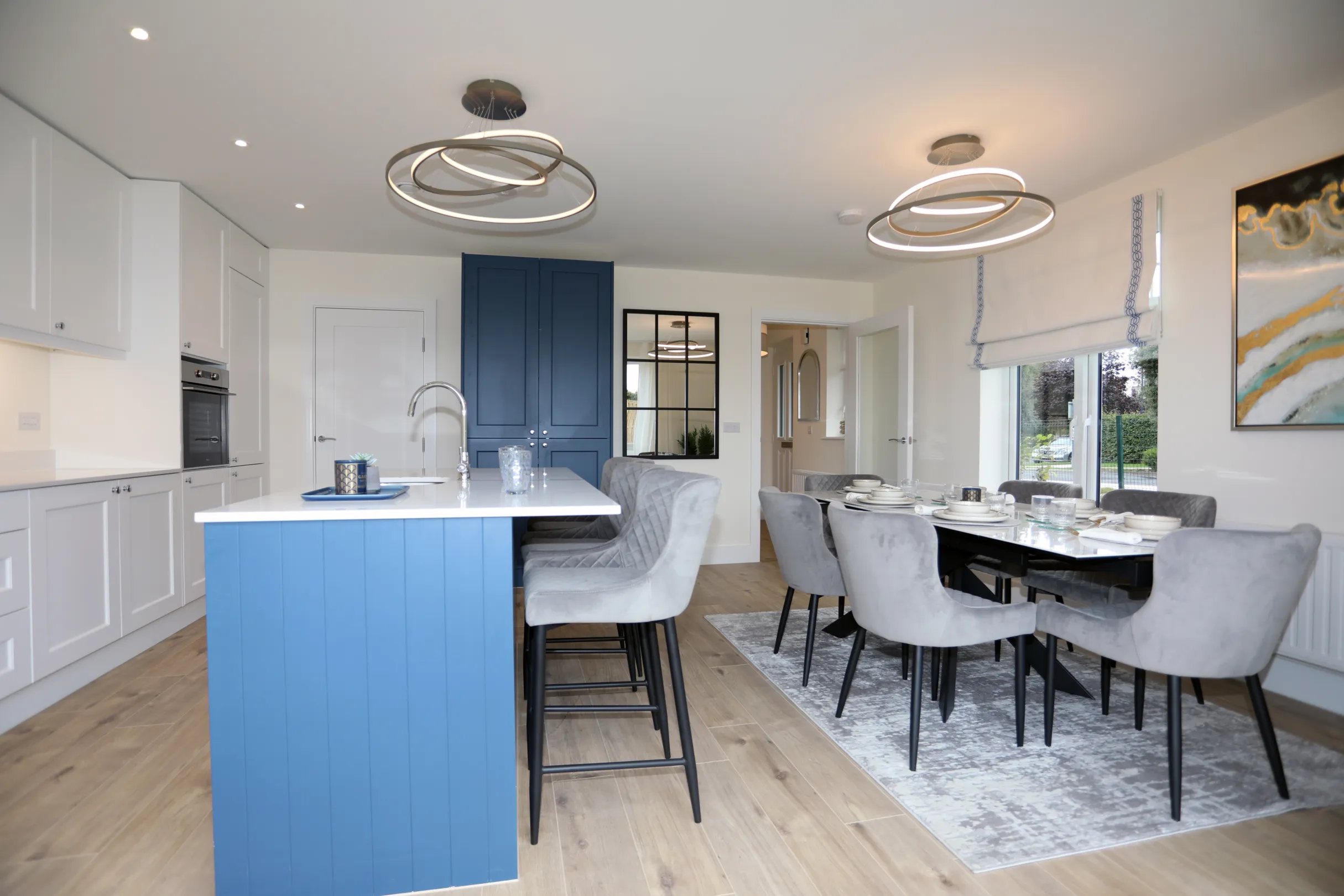 A modern kitchen dining room, a navy and white kitchen with central island unit, dining table set with plates and cutlery with grey dining chairs
