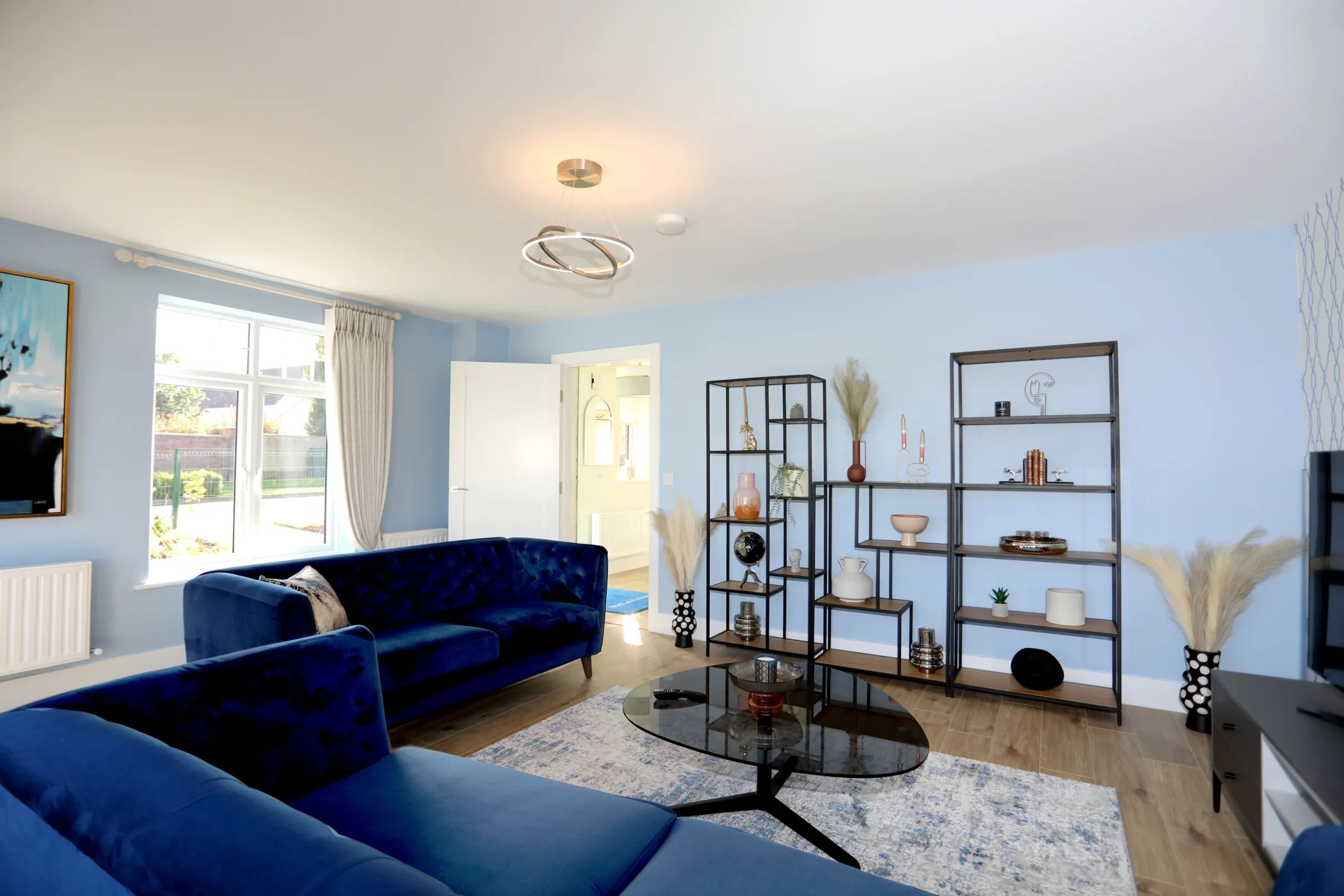 A modern living room with 2 navy blue sofas, a shelving rack with trinkets, coffee table, and TV unit