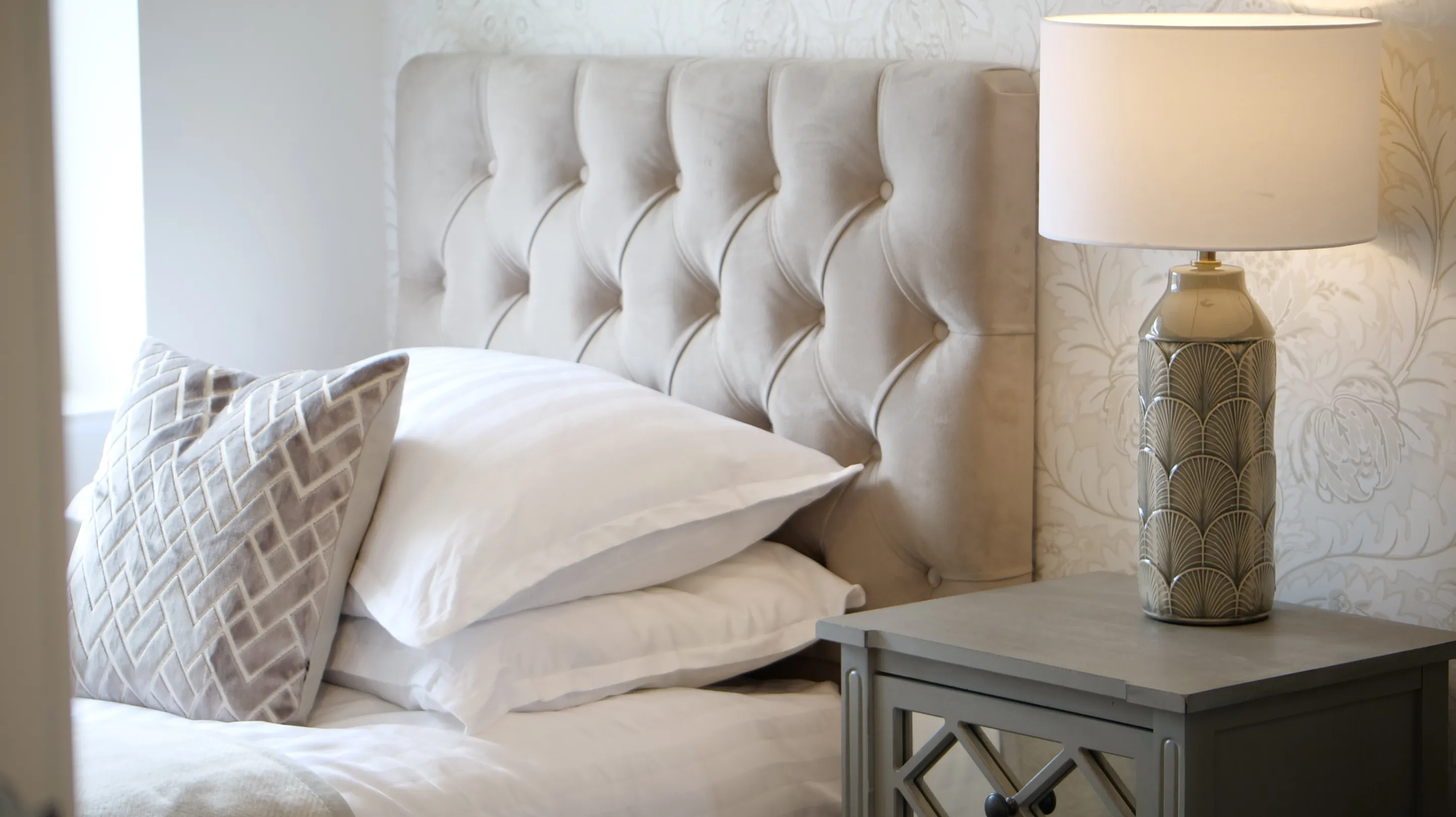 A close up image of a taupe headboard, bedside table and lamp