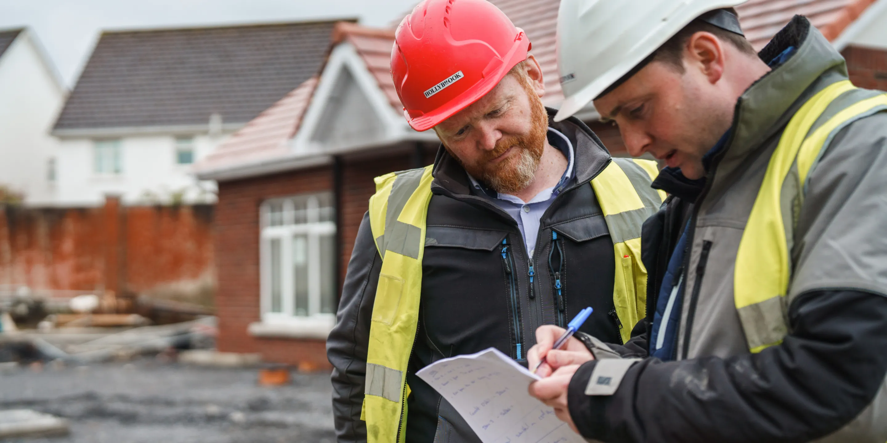 Two men on a building site wearing PPE marking up a programme
