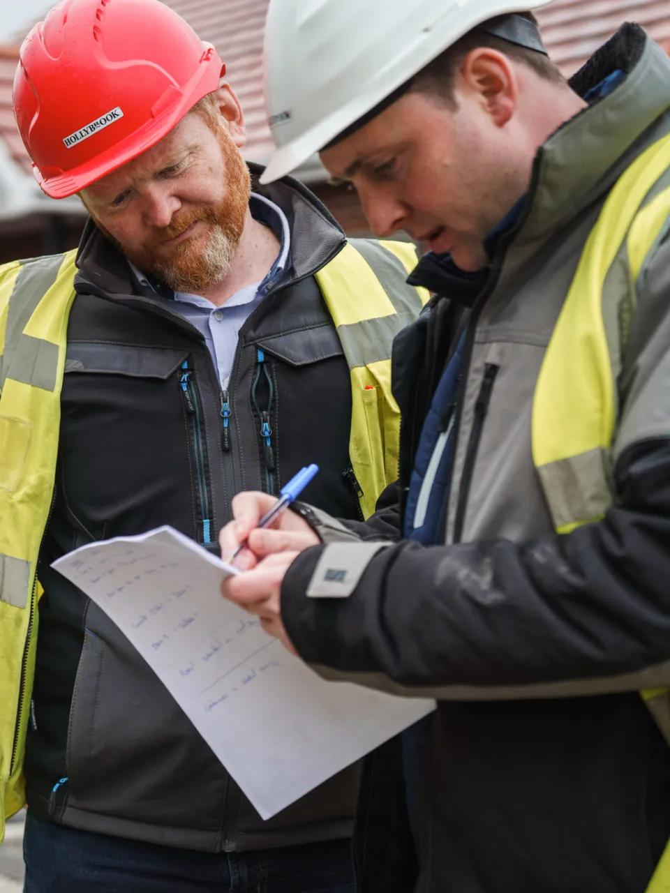 Two men on a building site wearing PPE marking up a programme