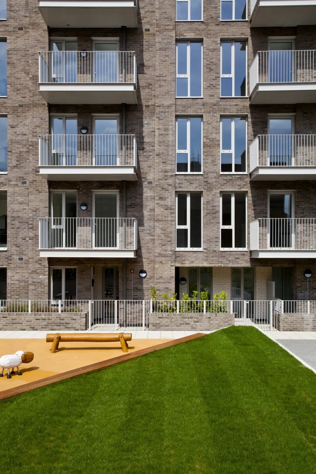 Detail modern multi storey residential building with balconies and a communal lawned and children's activity area in the foreground.