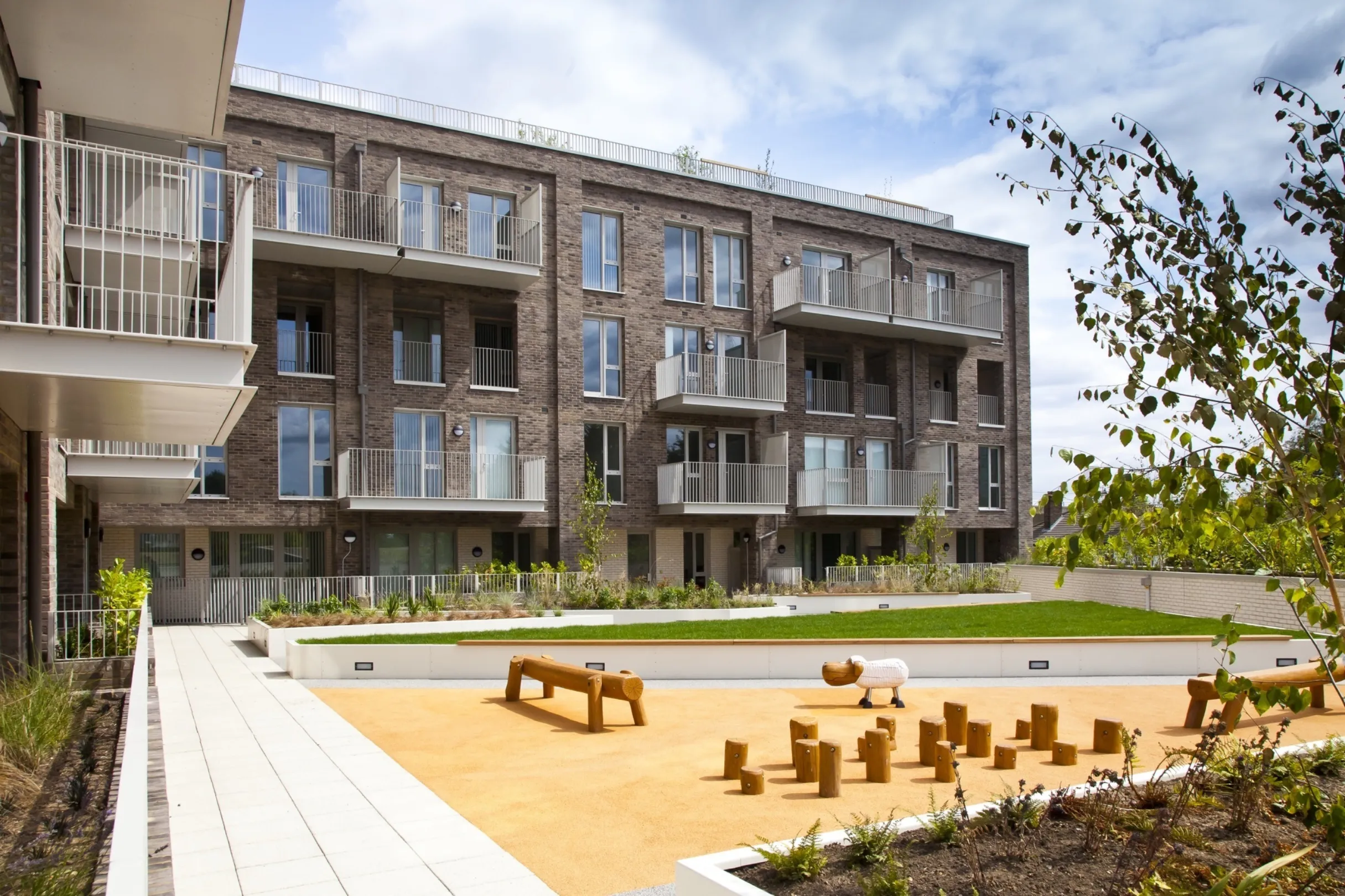 Detail modern multi storey residential building with balconies and a communal lawn and children's activity area in the foreground.