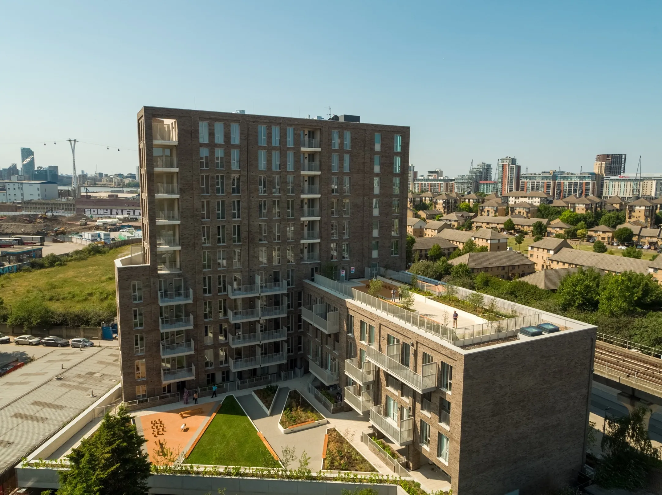 Arial view of a multi-level, multi story residential development showing two levels of communal roof gardens. The London cable car is visible in the distance.