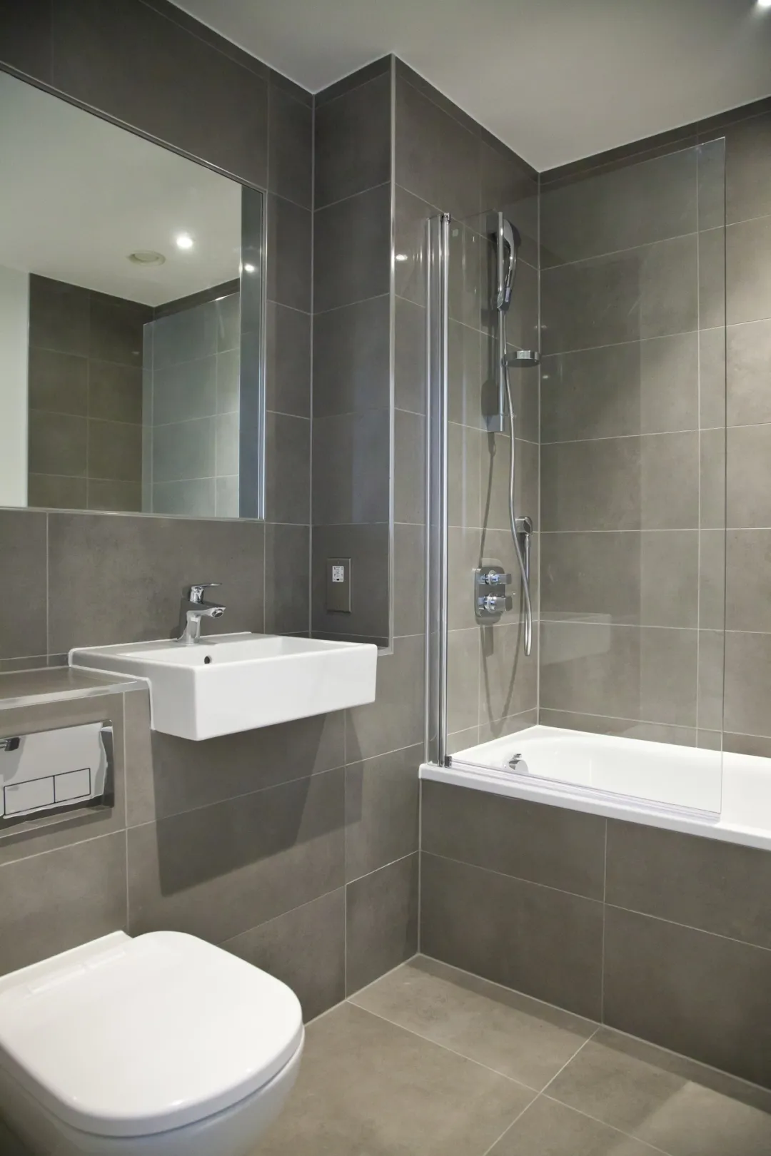 A modern fitter tiled bathroom with glazed shower screen on the bath and a large vanity mirror.