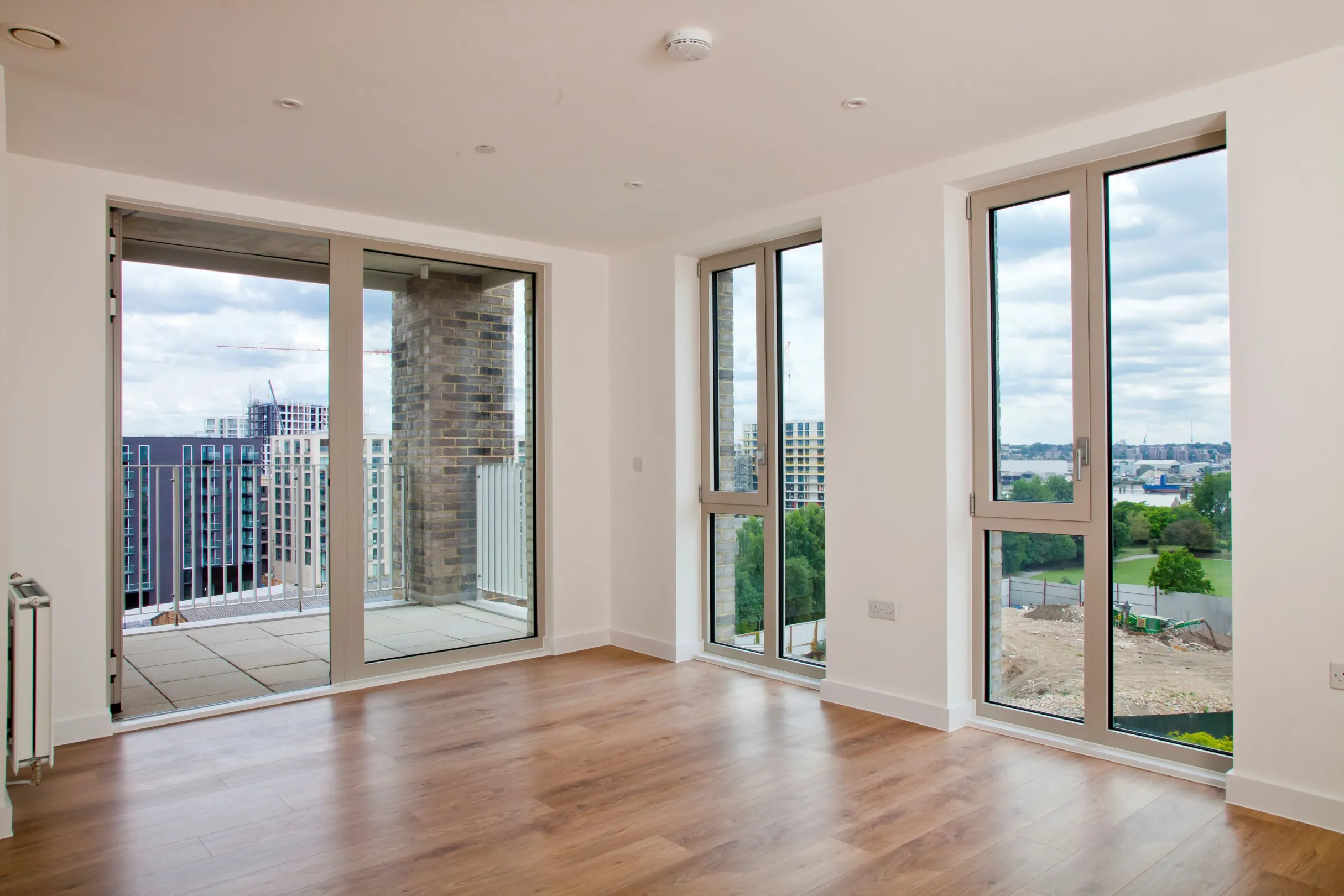 New build development, showing a living room area with hard wood flooring and full height, floor to ceiling, windows and a balcony
