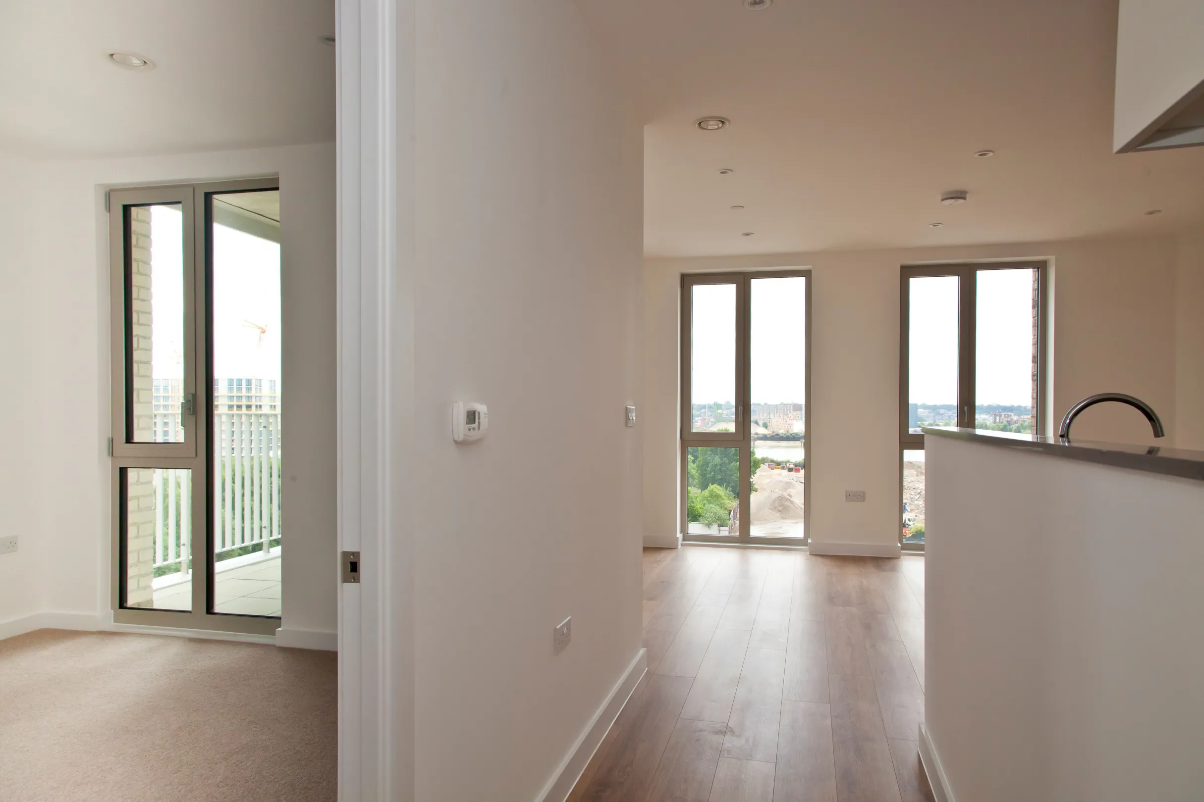 New build development, showing a glimpse into a bedroom, living room and kitchen area with hard wood flooring and full height, floor to ceiling, windows