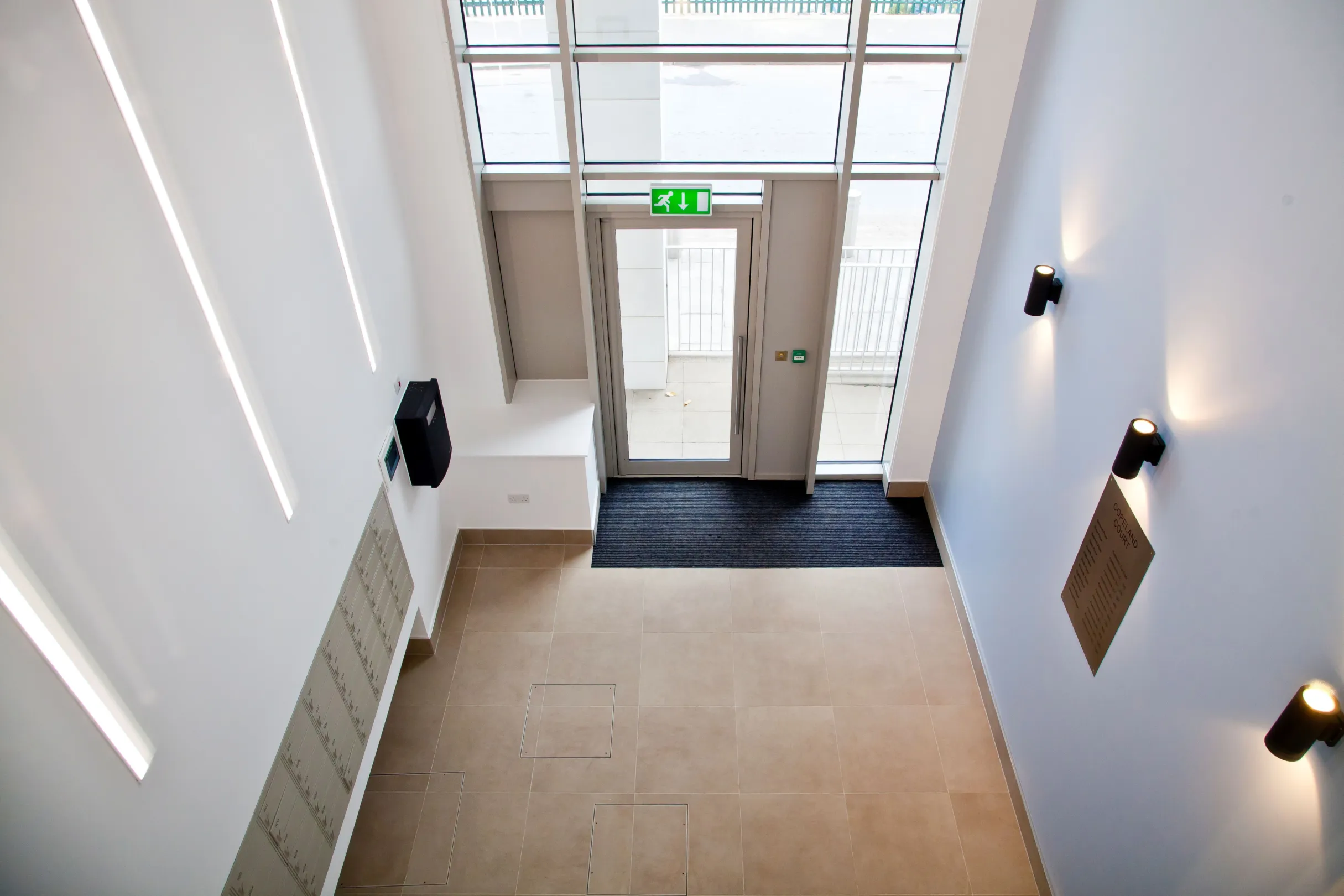 Double height foyer of a new build block of flats, showing wall lights and letterboxes